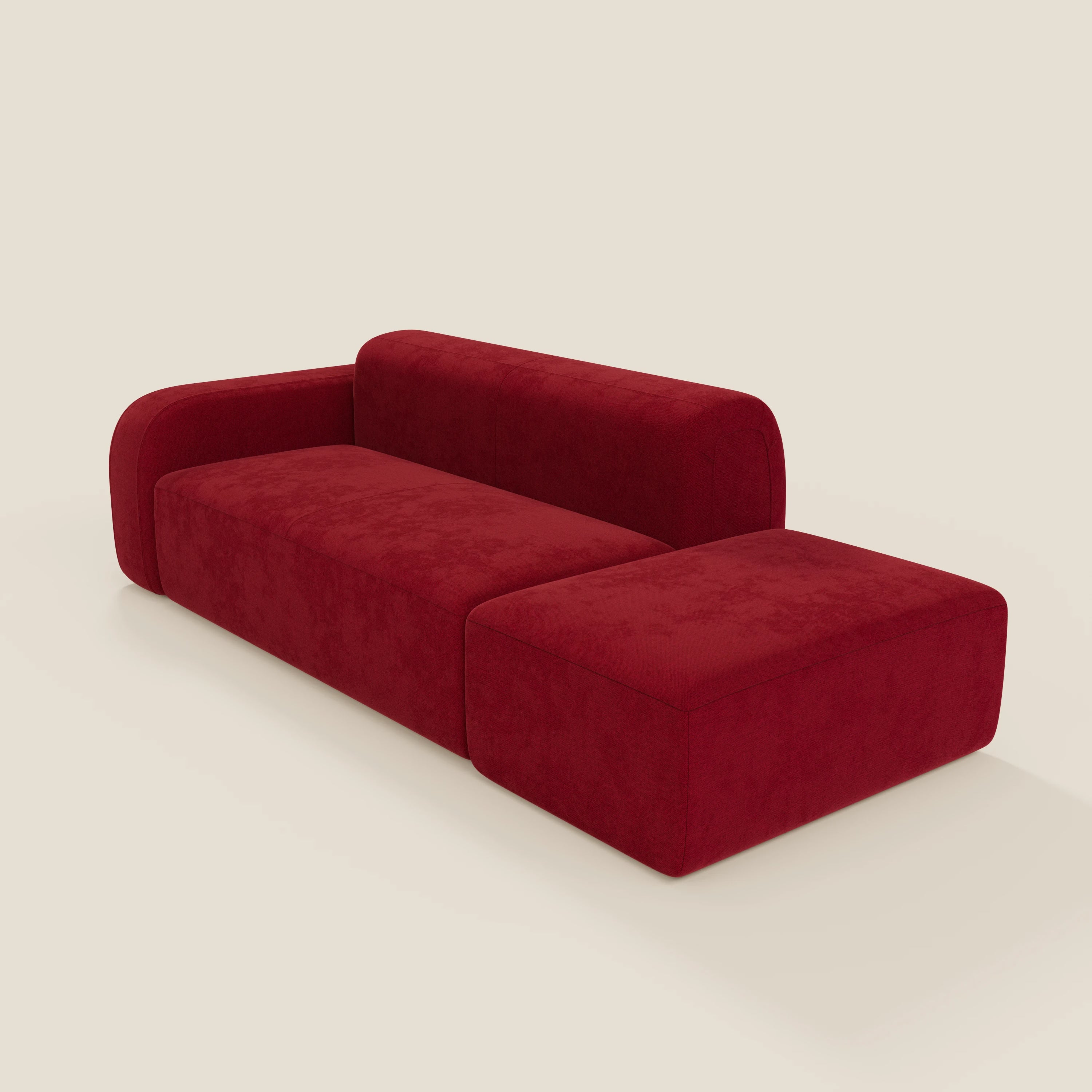 Il BonBon Divano componibile di Divani.Store in smacchiabile T23 bordeaux è caratterizzato da una seduta bassa e rettangolare, un bracciolo sinistro arrotondato, una chaise lounge annessa e un pouf terminale destro abbinato su uno sfondo bianco sporco.