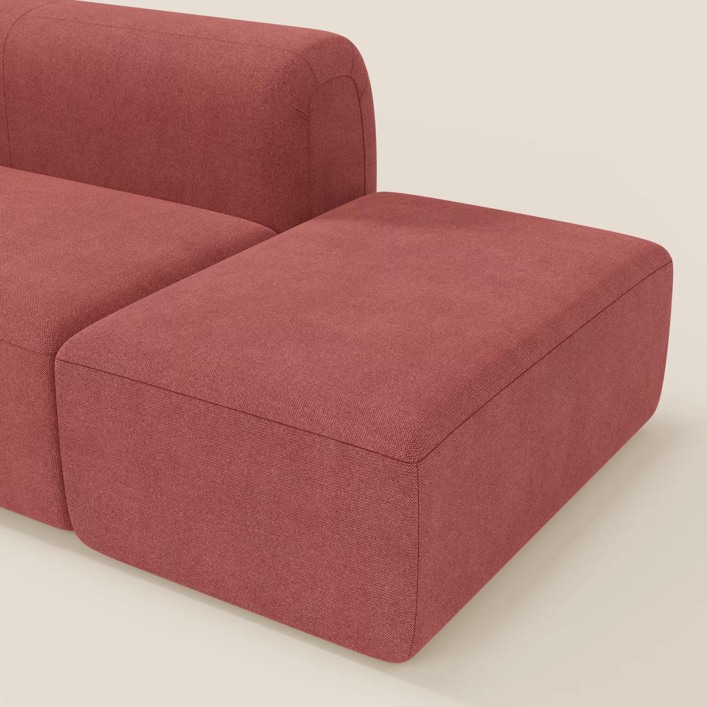 Il BonBon Divano componibile di Divani.Store è caratterizzato da una sezione con bracciolo a sinistra e da un ampio pouf rettangolare all'estremità destra in tessuto T23 antimacchia rosso ciliegia, presentato su uno sfondo bianco sporco.