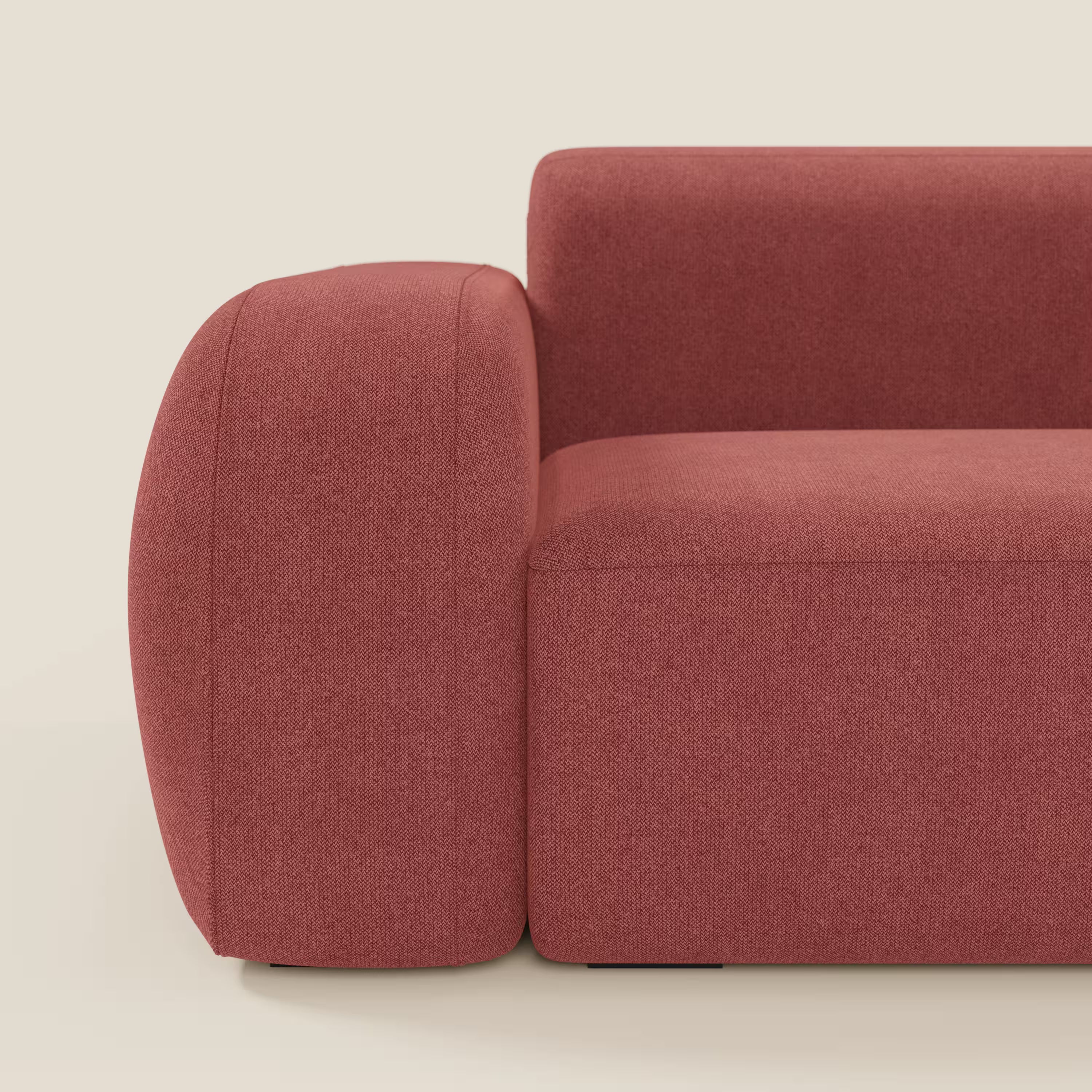 Primo piano del divano componibile BonBon di Divani.Store in tessuto smacchiabile T23 rosso ciliegia, con ampio bracciolo arrotondato e spesso cuscino di seduta. Design minimalista e squadrato; sono visibili solo il lato sinistro e parte dello schienale.