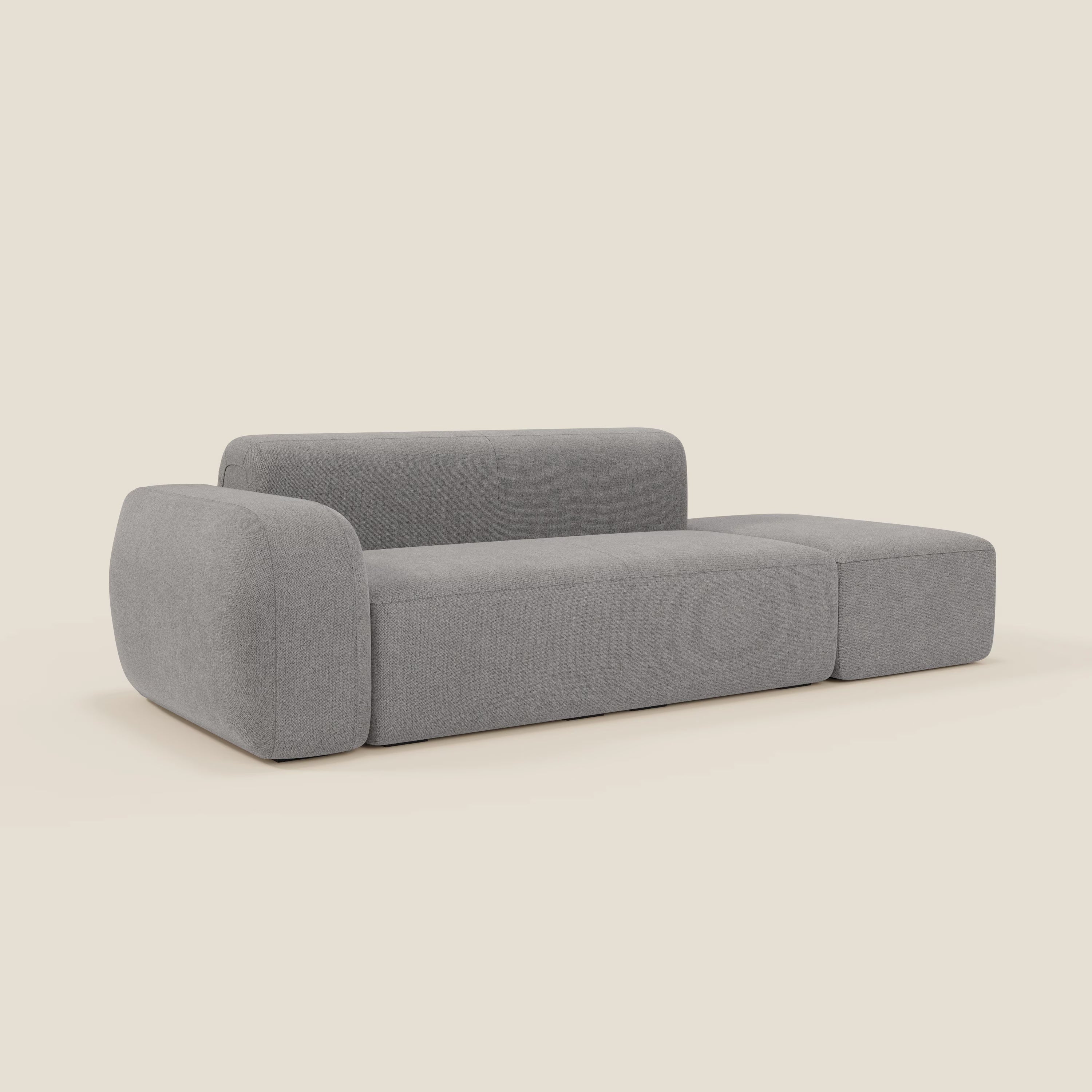 Il BonBon Divano componibile di Divani.Store è caratterizzato da un design minimalista con schienale basso in tessuto antimacchia grigio T23, ampio bracciolo sinistro, cuscini spessi e seduta a livello del pavimento. Presentato su sfondo beige chiaro con pouf terminale.