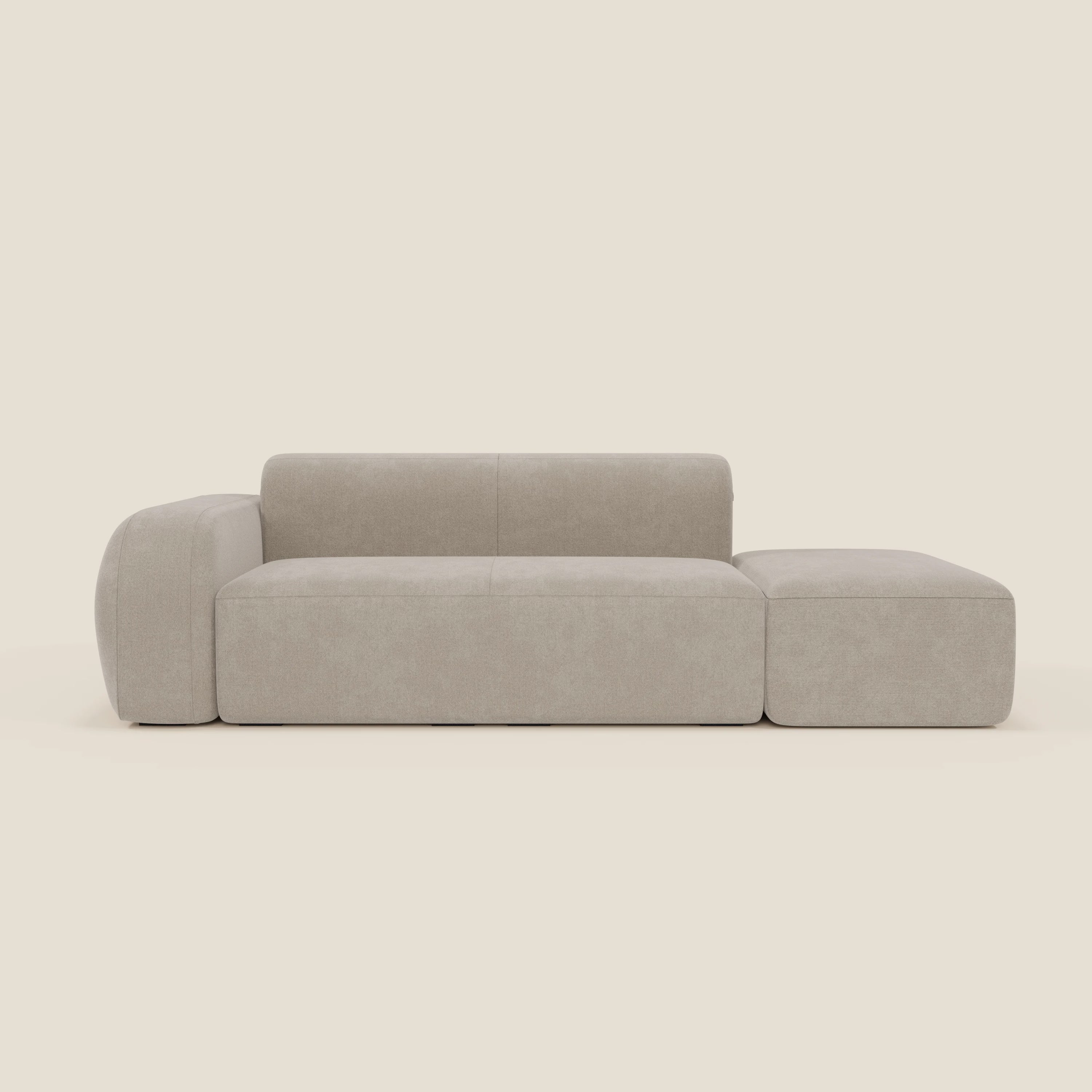 Il BonBon Divano componibile di Divani.Store, in tessuto antimacchia T23 panna, è dotato di bracciolo sinistro e pouf terminale destro; il suo design minimalista beige si staglia su uno sfondo crema chiaro.