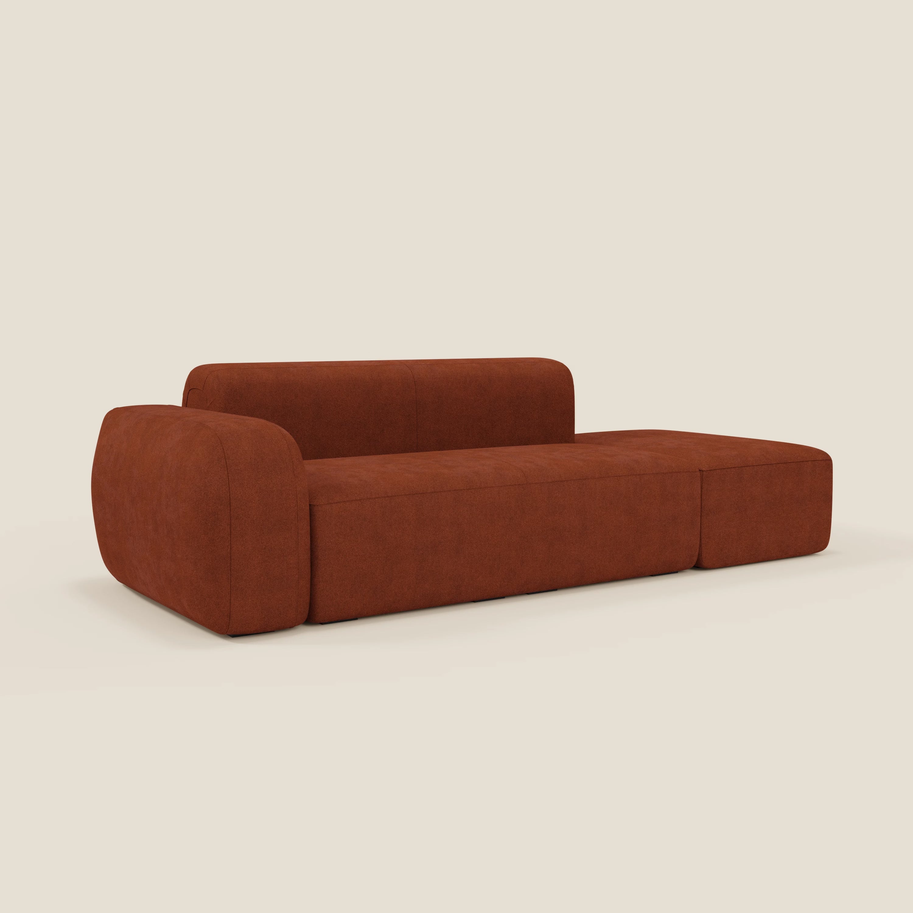 Il Divano componibile BonBon di Divani.Store è caratterizzato da un design morbido e a basso profilo in tessuto antimacchia T23 ruggine, con bracciolo sinistro e pouf terminale destro, su uno sfondo semplice color crema.