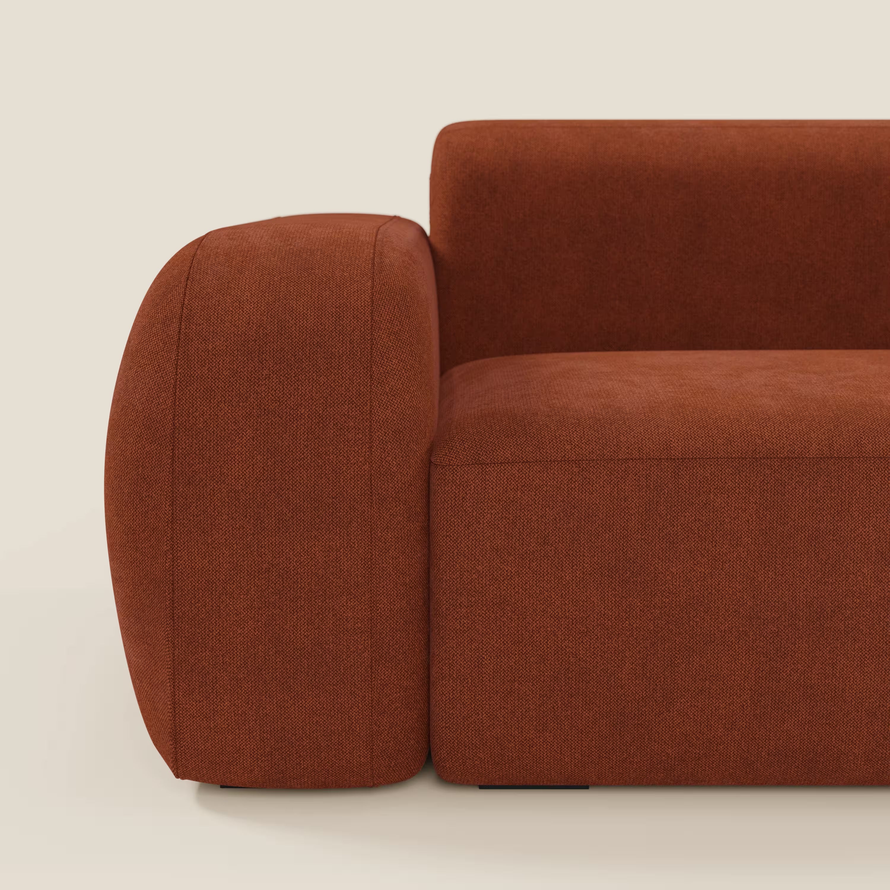 Primo piano del modulare componibile BonBon Divano di Divani.Store in smacchiabile ruggine T23, che mostra il bracciolo sinistro, la seduta e lo schienale con bordi morbidi e arrotondati e un design minimalista su uno sfondo beige chiaro.