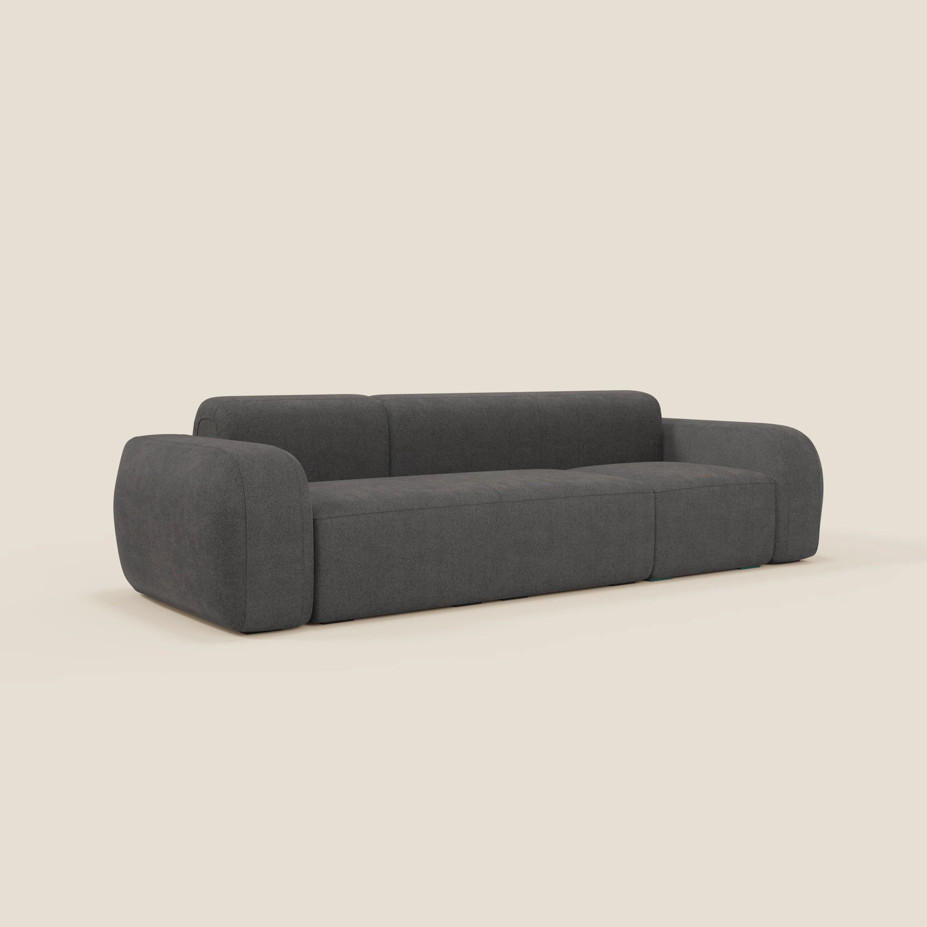Il BonBon Divano componibile di Divani.Store, in tessuto smacchiabile T23 antracite, presenta un design moderno e minimalista con bordi morbidi e arrotondati, uno schienale basso e tre posti a sedere. In un'ambientazione beige chiaro.