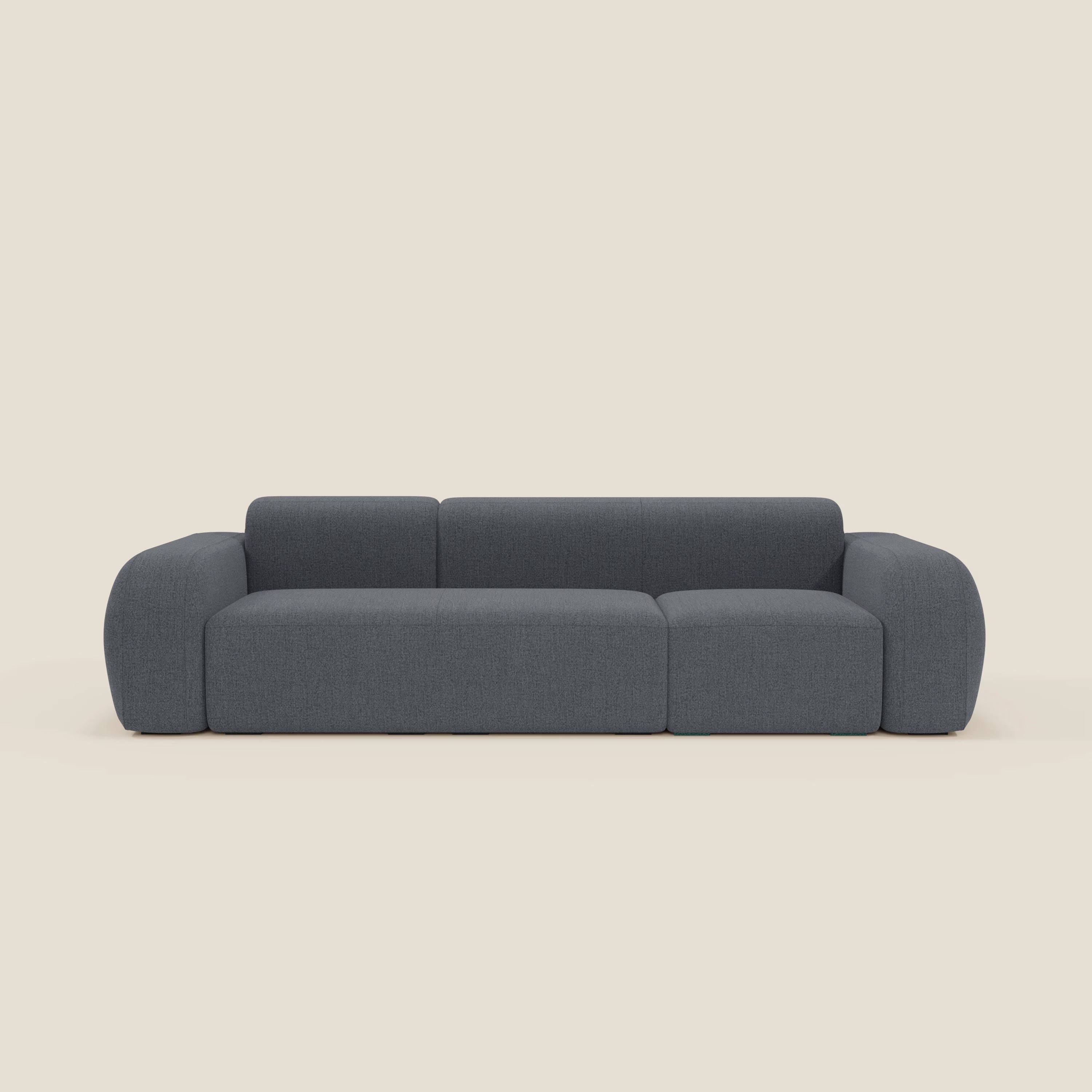 Il BonBon Divano componibile - Composizione Spaccamattone di Divani.Store in smacchiabile T23 blu grafite presenta un design moderno e di basso profilo con ampi braccioli arrotondati, tre sezioni di seduta e uno schienale continuo su uno sfondo beige chiaro.