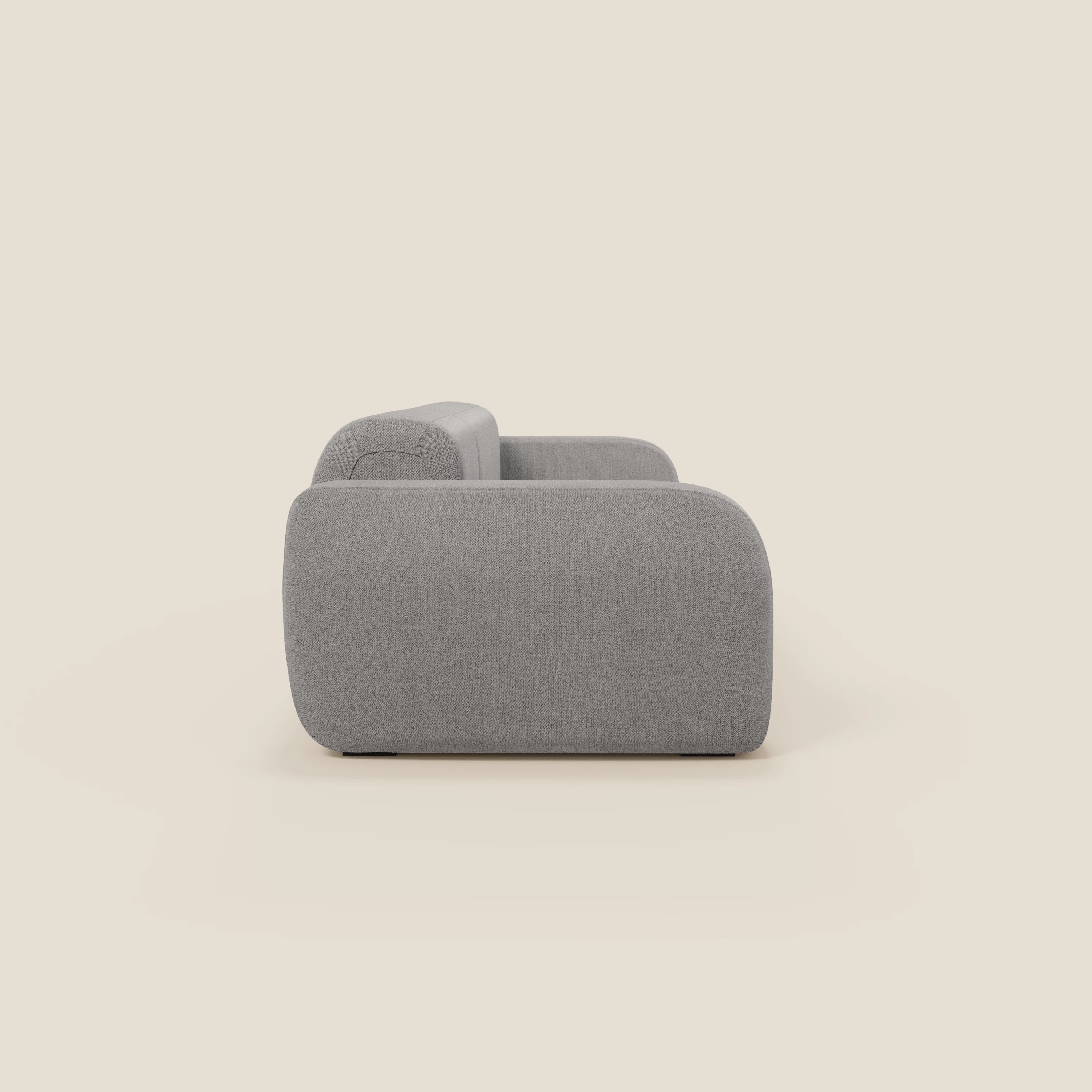 Una vista laterale del BonBon Divano modulare componibile - Composizione Spaccamattone di Divani.Store, in tessuto smacchiabile T23 grigio, con bordi arrotondati e schienale basso, mostra uno stile minimalista e contemporaneo su uno sfondo beige chiaro.