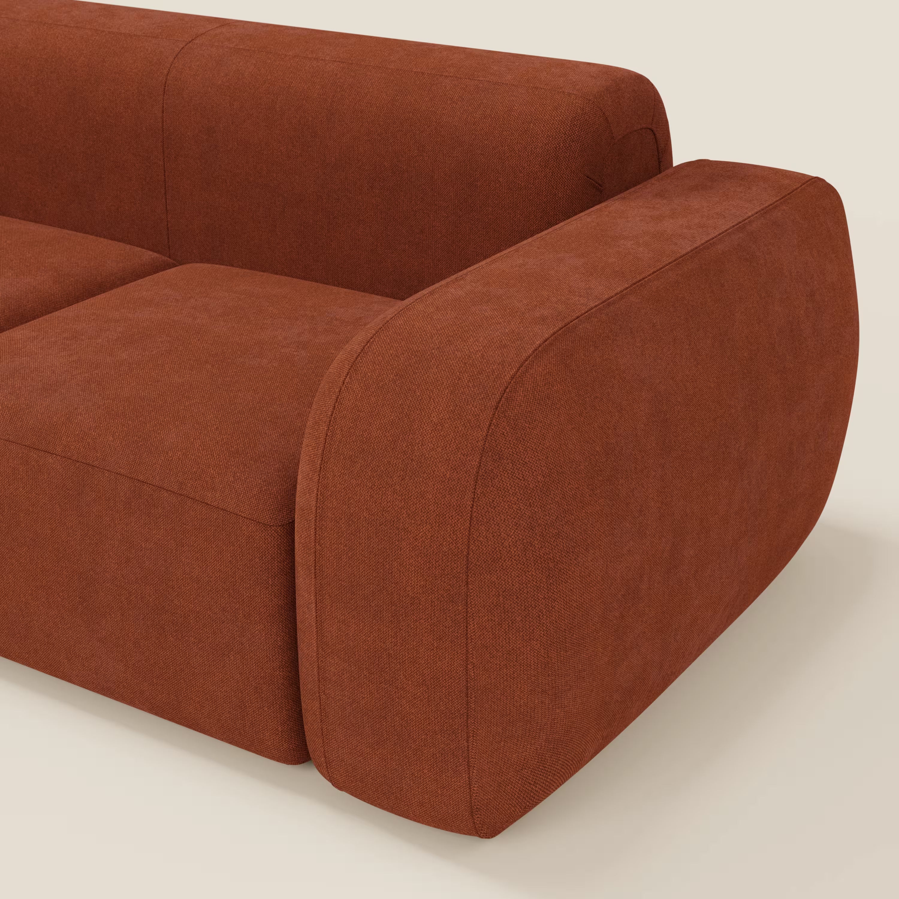 Primo piano del divano componibile BonBon Divano - Composizione Spaccamattone in tessuto smacchiabile T23 di Divani.Store, caratterizzato da tessuto color ruggine e braccioli spessi e arrotondati su uno sfondo bianco sporco.