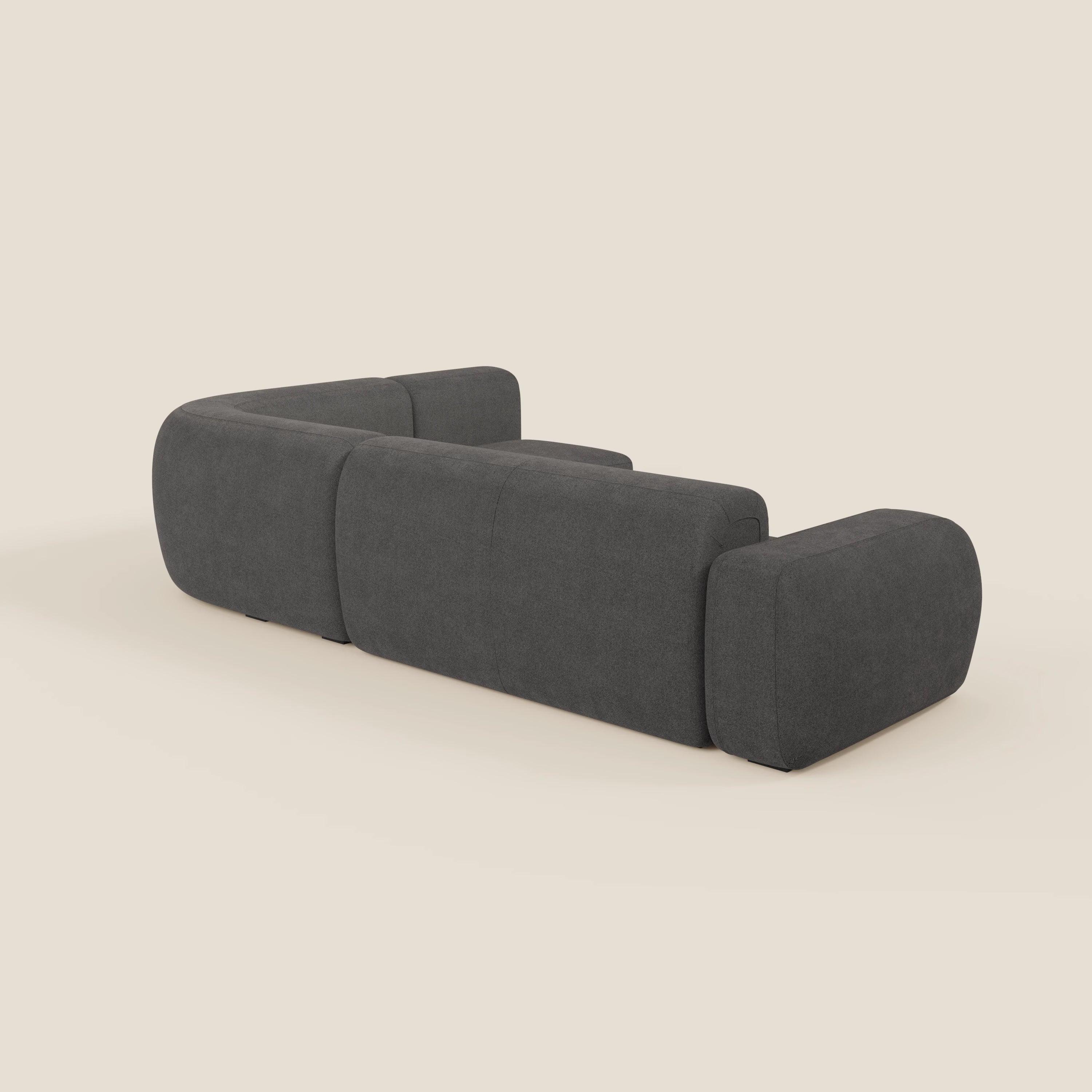 Il divano angolare componibile e modulare BonBon di Divani.Store, presentato nella parte posteriore in tessuto smacchiabile T23 antracite, è caratterizzato da forme robuste, bordi arrotondati e un design minimalista su uno sfondo bianco sporco.