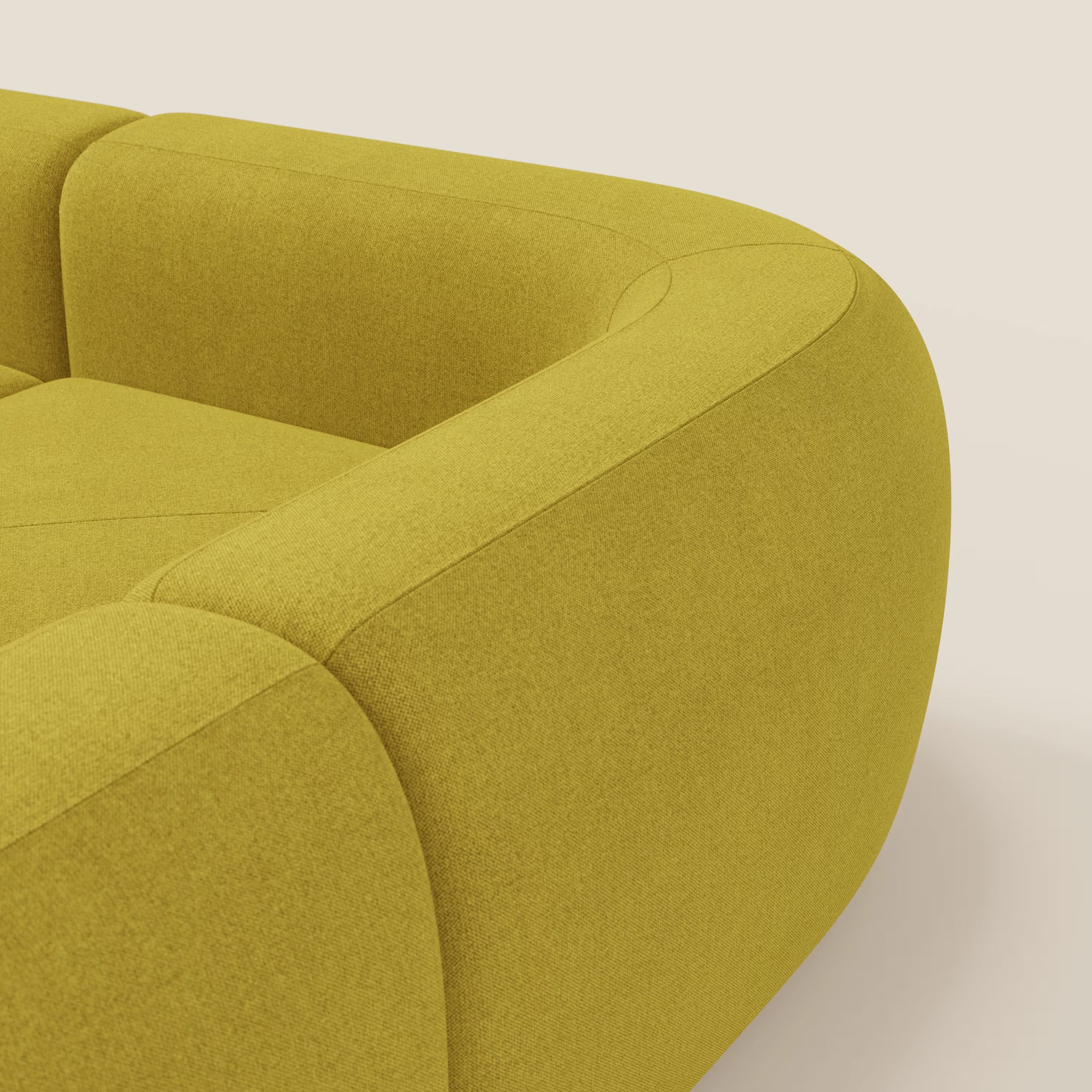 Primo piano del divano angolare componibile e modulare BonBon di Divani.Store, rivestito in tessuto smacchiabile T23 giallo sole con bordi arrotondati e ampi braccioli. Il design su misura e la texture morbida spiccano su uno sfondo color crema.