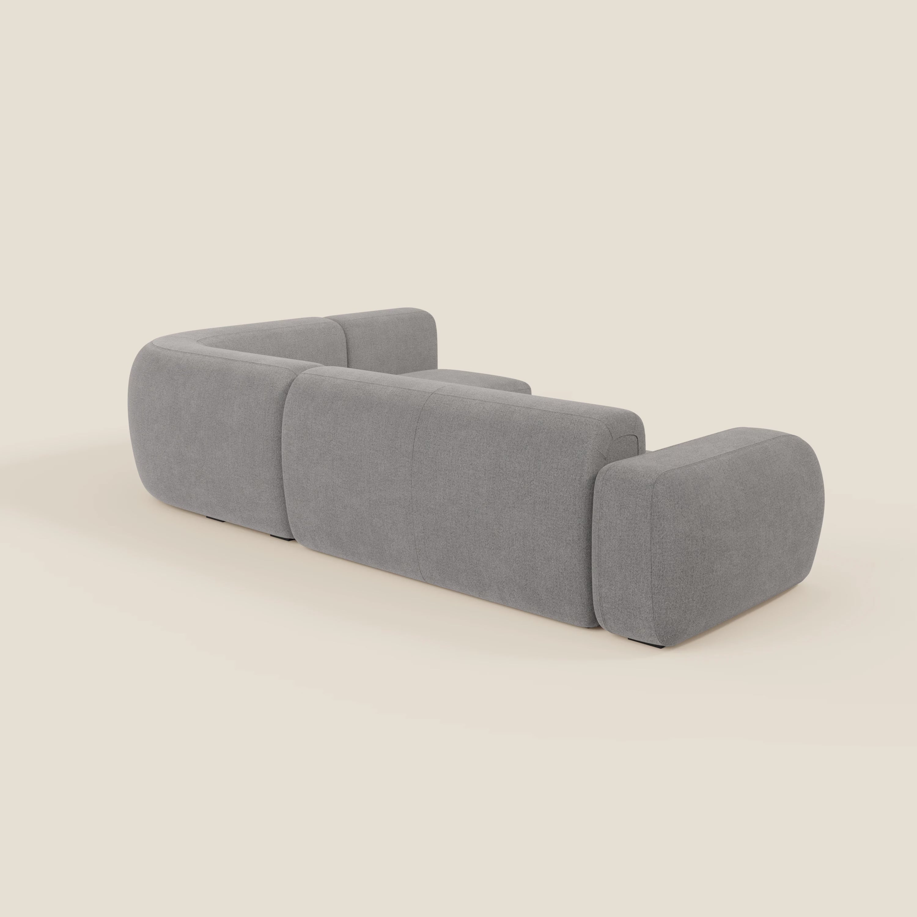 Il divano angolare componibile e modulare BonBon di Divani.Store, in tessuto smacchiabile T23 grigio, è caratterizzato da bordi lisci e arrotondati e da braccioli e schienale morbidi, mostrati dal retro per evidenziare il suo design minimalista su uno sfondo bianco sporco.