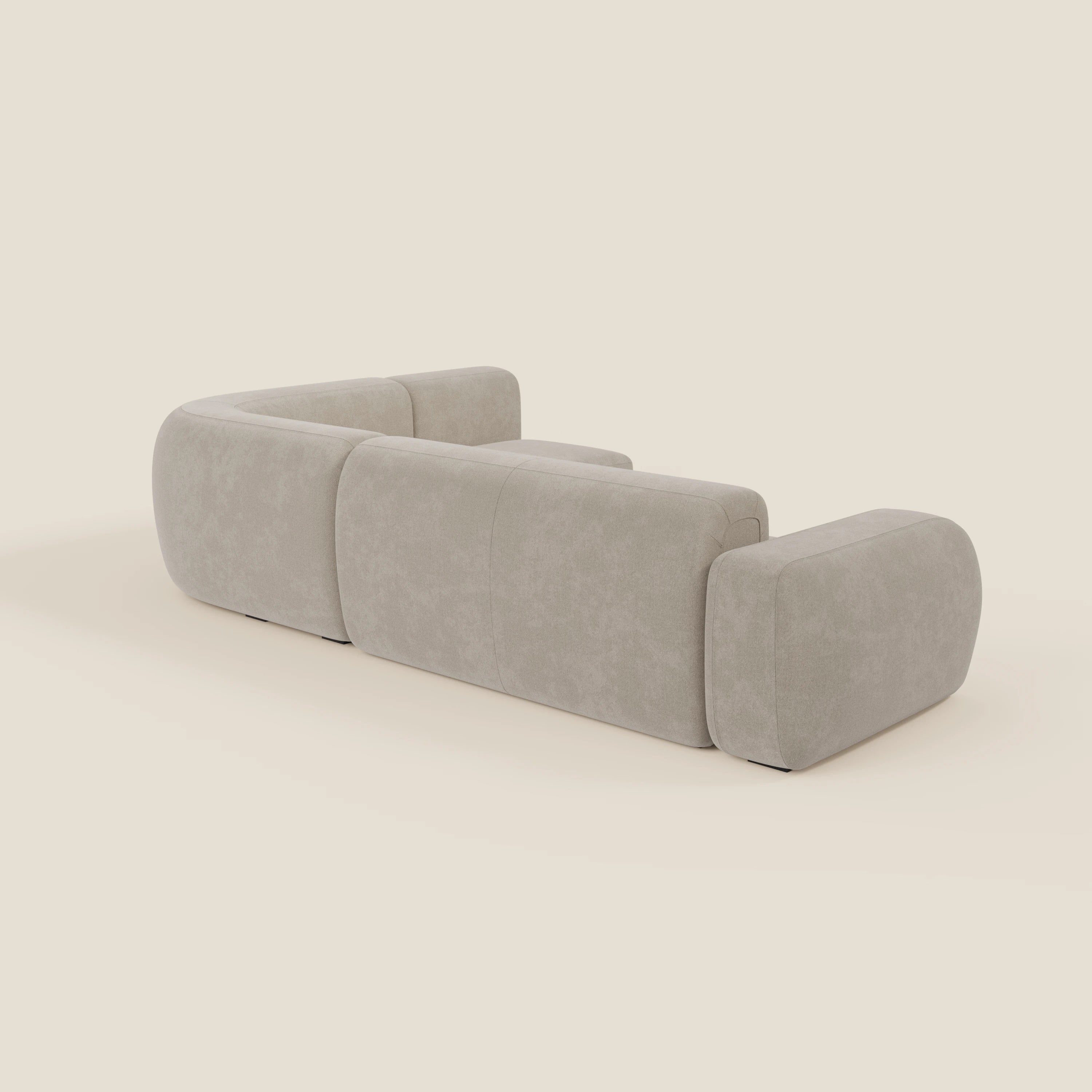 Il divano angolare componibile e modulare BonBon di Divani.Store, in tessuto smacchiabile T23 panna, è caratterizzato da un design moderno di colore beige con bordi arrotondati e tre sezioni principali imbottite, viste da dietro su un semplice sfondo crema.