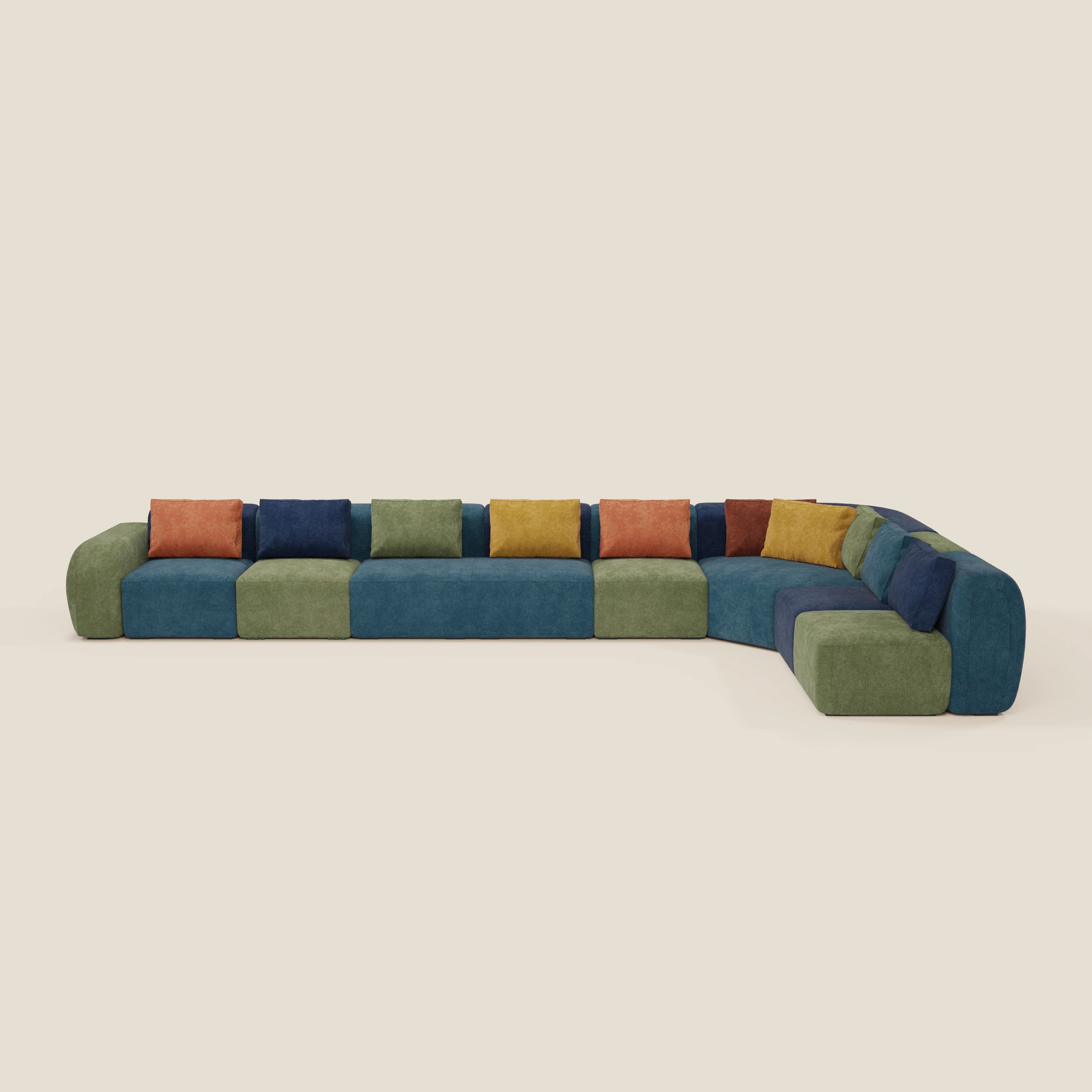 Il BonBon Grande Fratello Edition di Divani.Store è un grande divano modulare a forma di L con sezioni a blocchi verdi e blu, cuscini di seduta multipli e cuscini quadrati colorati in arancione, blu, rosso, verde e giallo su uno sfondo beige semplice.