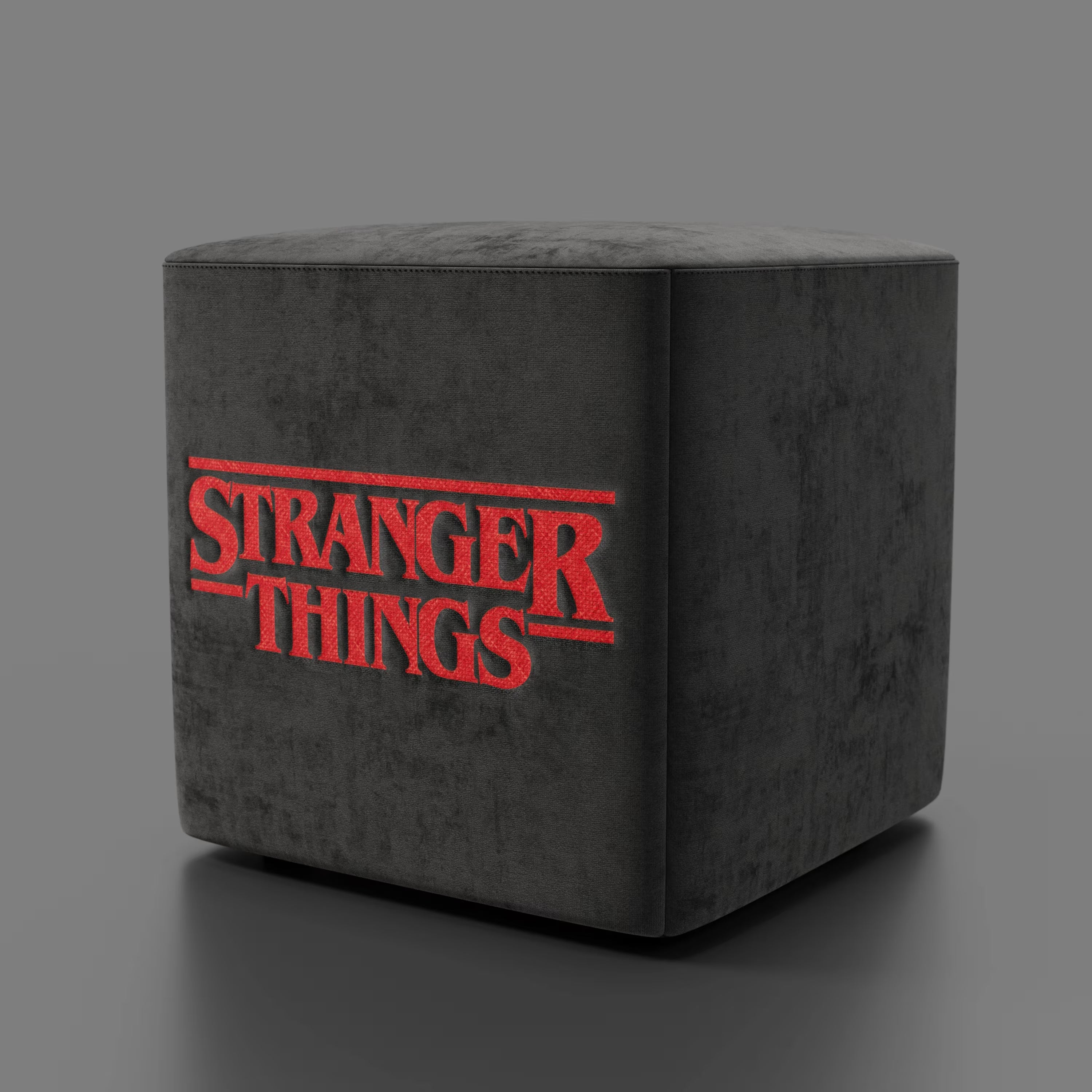Il pouf Cube Stranger Things Edition di Divani.Store è caratterizzato da un tessuto antracite antimacchia e dall'audace logo rosso sul davanti, che combina un comfort morbido e felpato con linee moderne, qui raffigurate su uno sfondo grigio semplice.