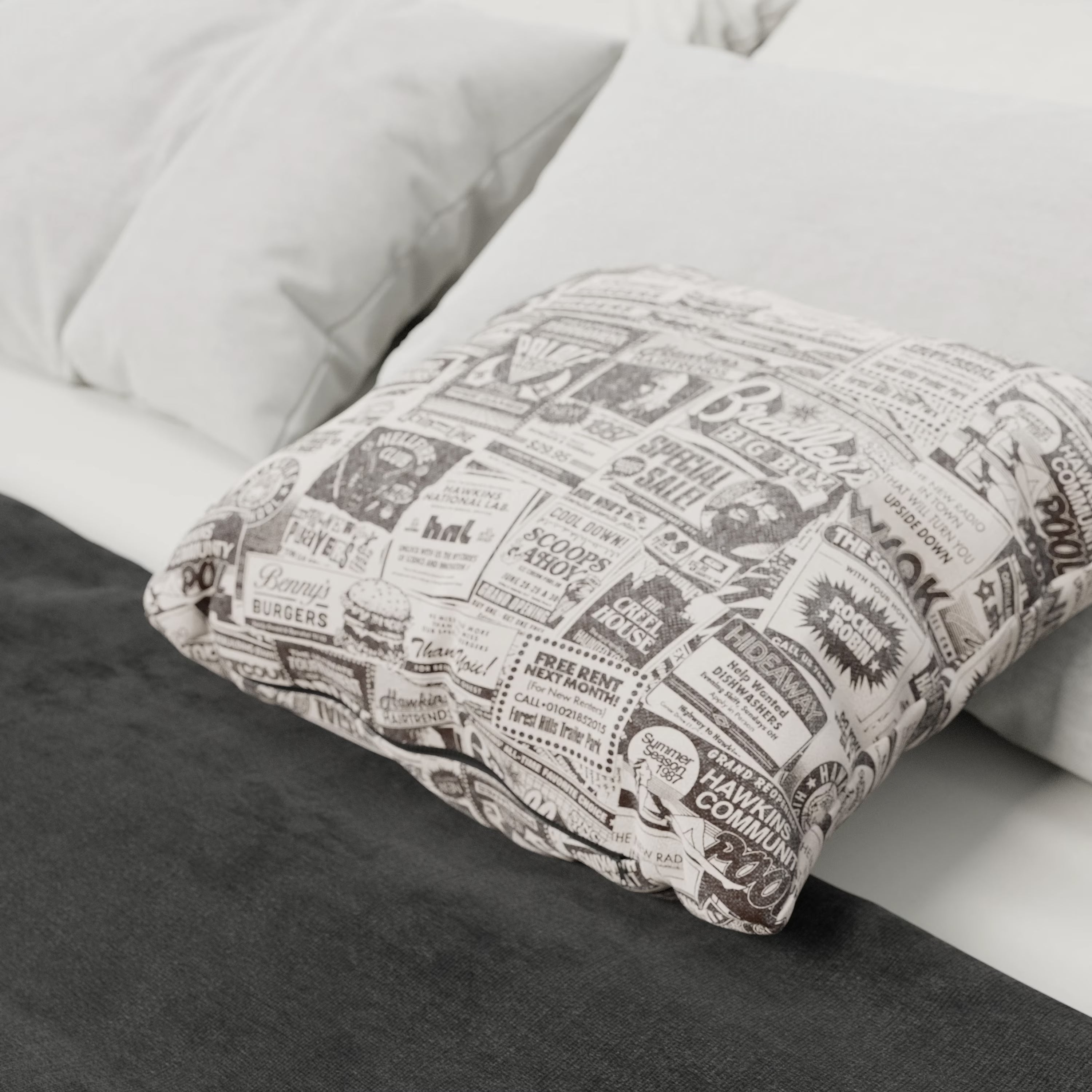 Un letto con cuscini bianchi è abbinato al cuscino Divani.Store Hawkins Post Stranger Things - Limited Edition 45x45 cm, con stampa vintage in bianco e nero. Una coperta grigio scuro ai piedi aggiunge un'atmosfera accogliente e moderna.