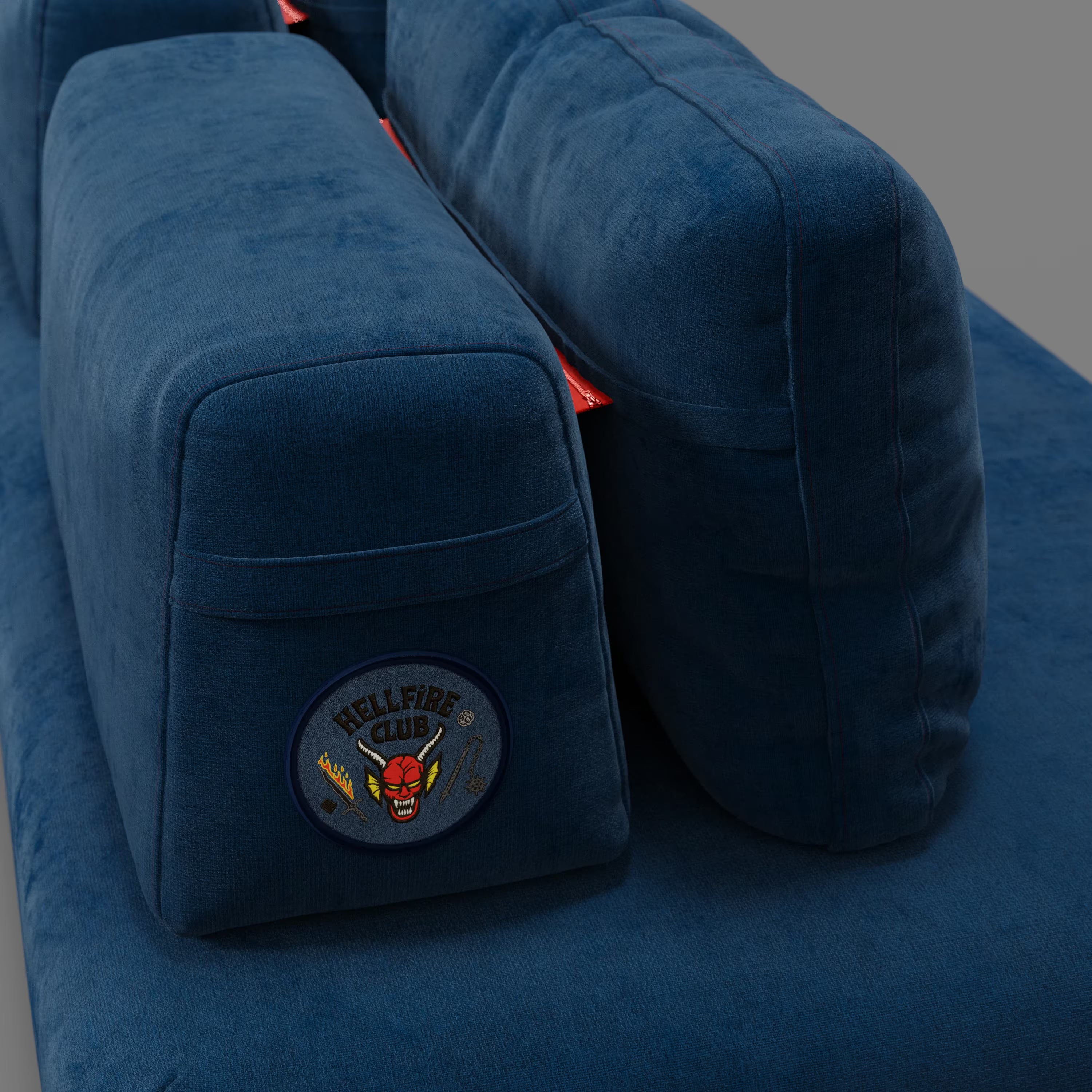 Primo piano del divano letto matrimoniale Rift STRANGER THINGS Edition di Divani.Store in tessuto blu antimacchia, con ampi braccioli. Uno di essi presenta una toppa "Hellfire Club". Lo sfondo grigio semplice ne evidenzia la consistenza e il colore.