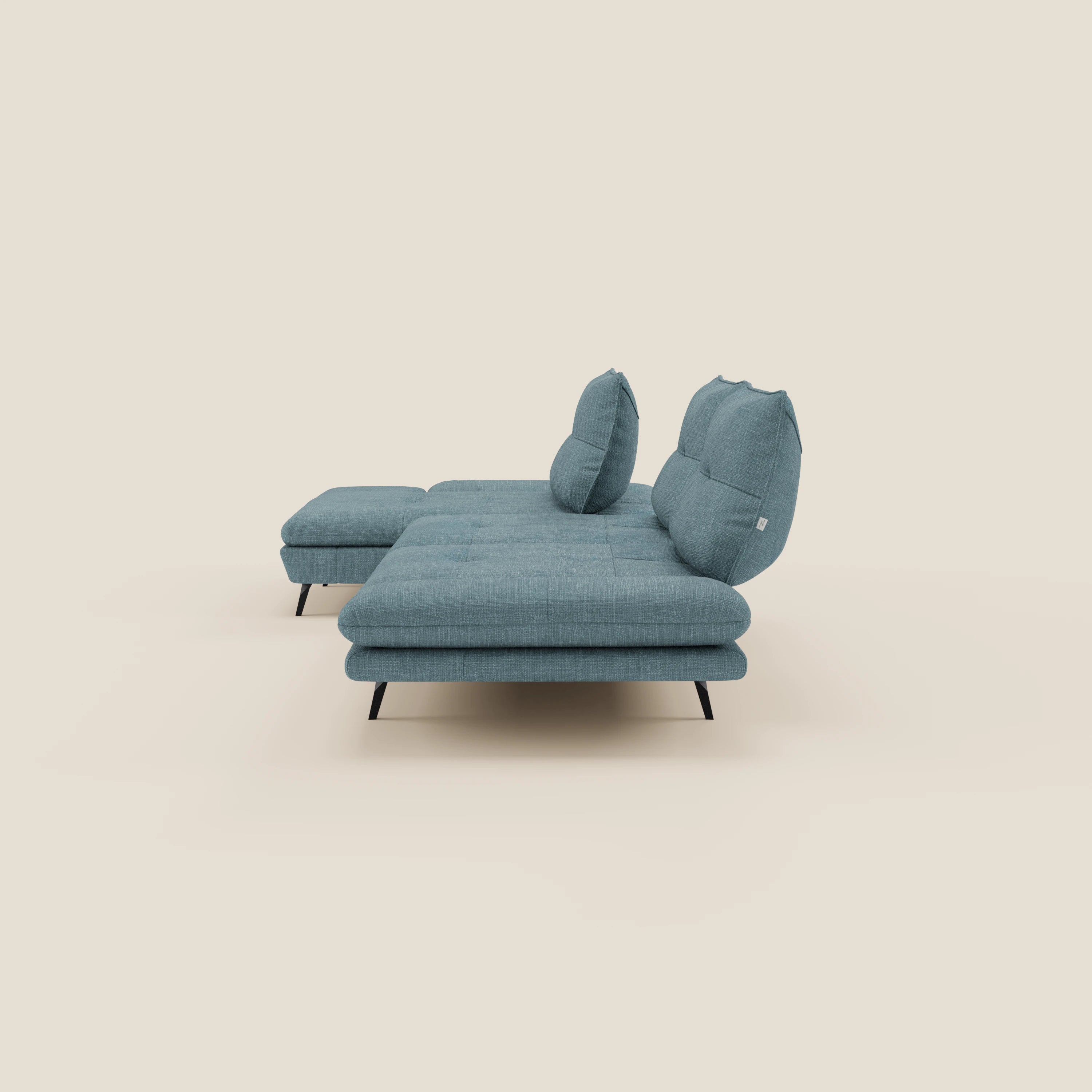 Il Divano con penisola Ardex di Divani.Store è caratterizzato da schienali traslanti, braccioli regolabili e un pouf coordinato in elegante tessuto impermeabile T06 azzurro con eleganti gambe nere, su uno sfondo beige chiaro.