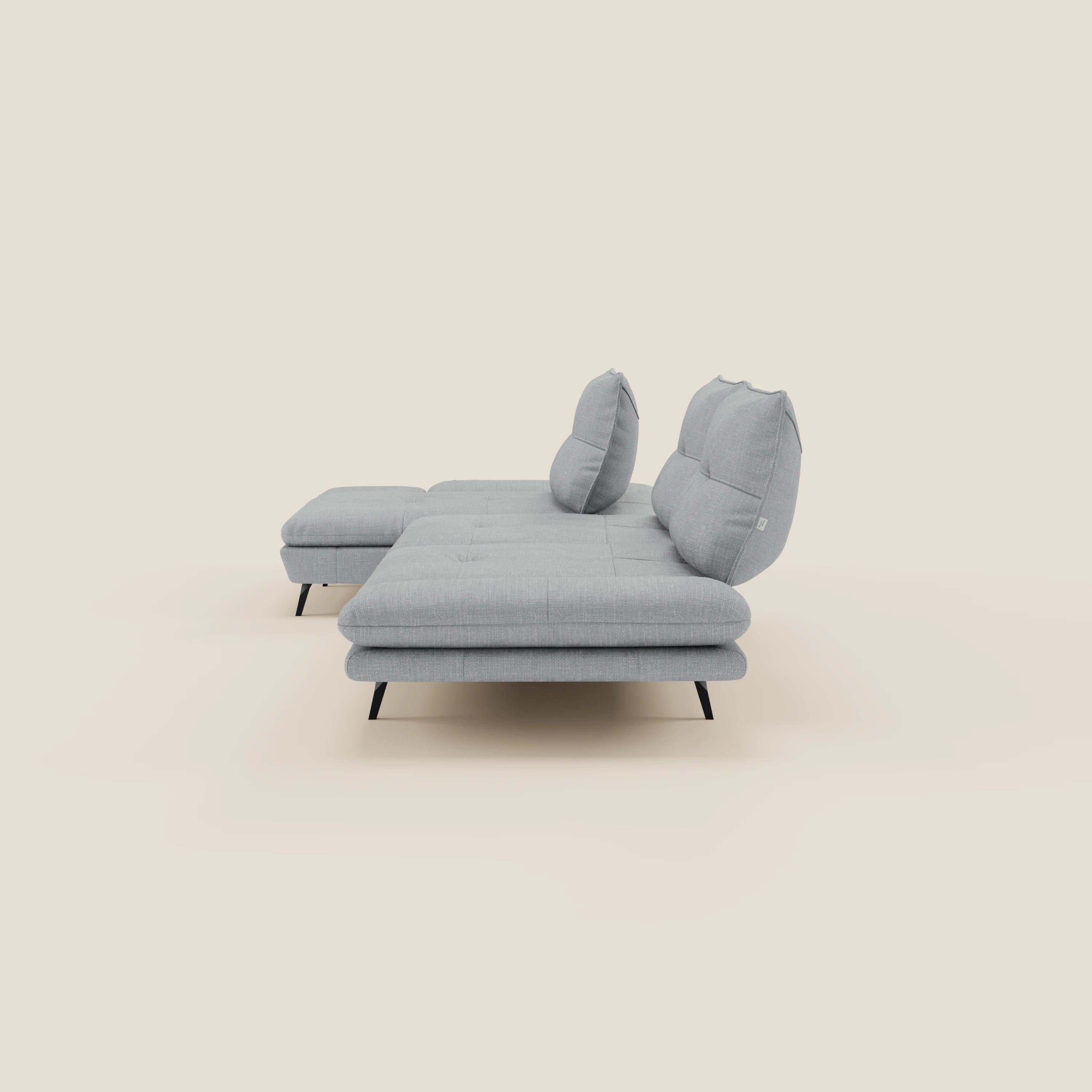 Il Divano con penisola Ardex di Divani.Store è caratterizzato da schienali traslanti, braccioli regolabili e due schienali in elegante tessuto impermeabile T06 ghiaccio con pouf e sottili gambe nere, su uno sfondo bianco sporco.