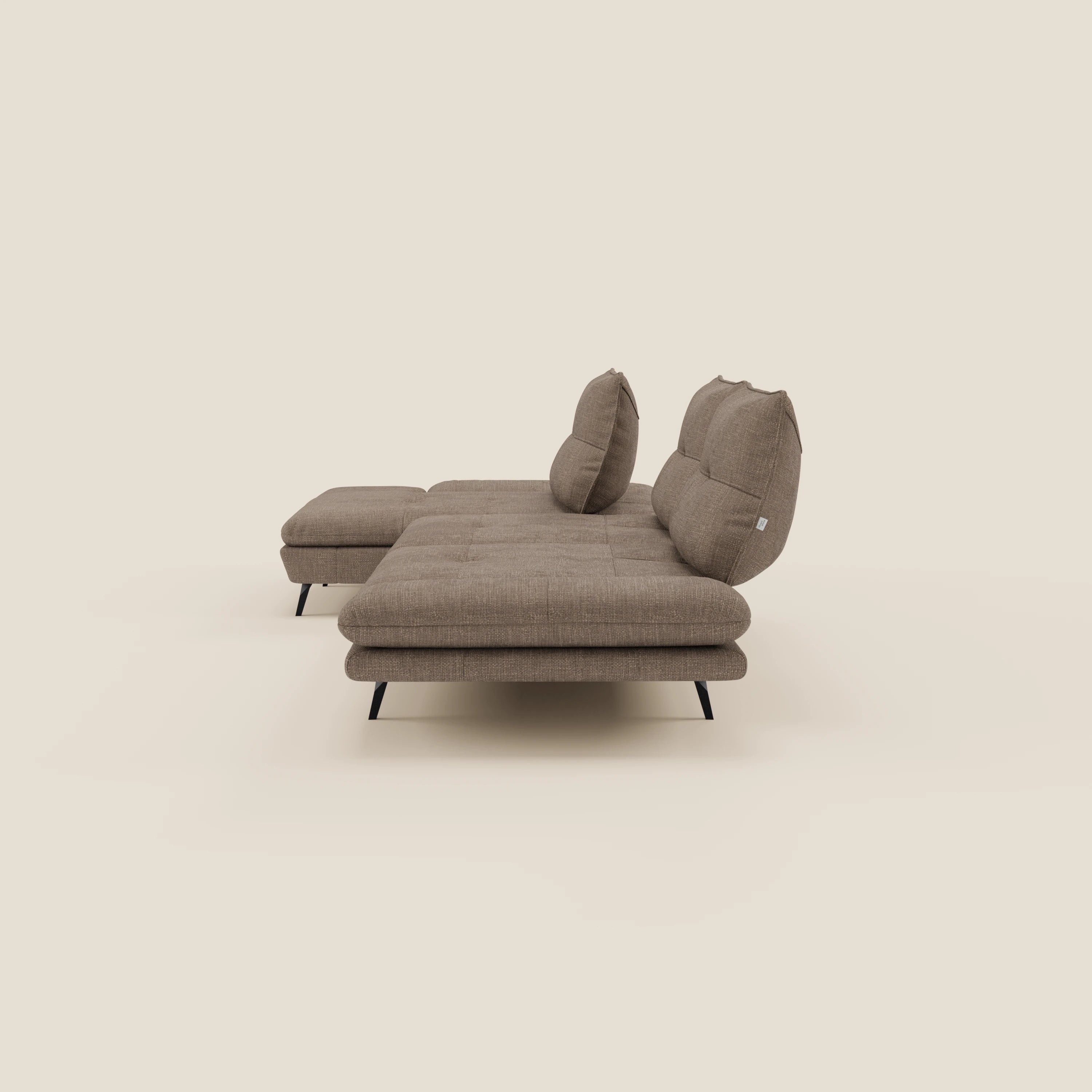 Il Divano con penisola Ardex di Divani.Store è caratterizzato da schienali traslanti, braccioli regolabili e cuscini trapuntati in elegante tessuto impermeabile T06 marrone. Include un pouf sinistro coordinato e sottili gambe in metallo nero, su uno sfondo beige.