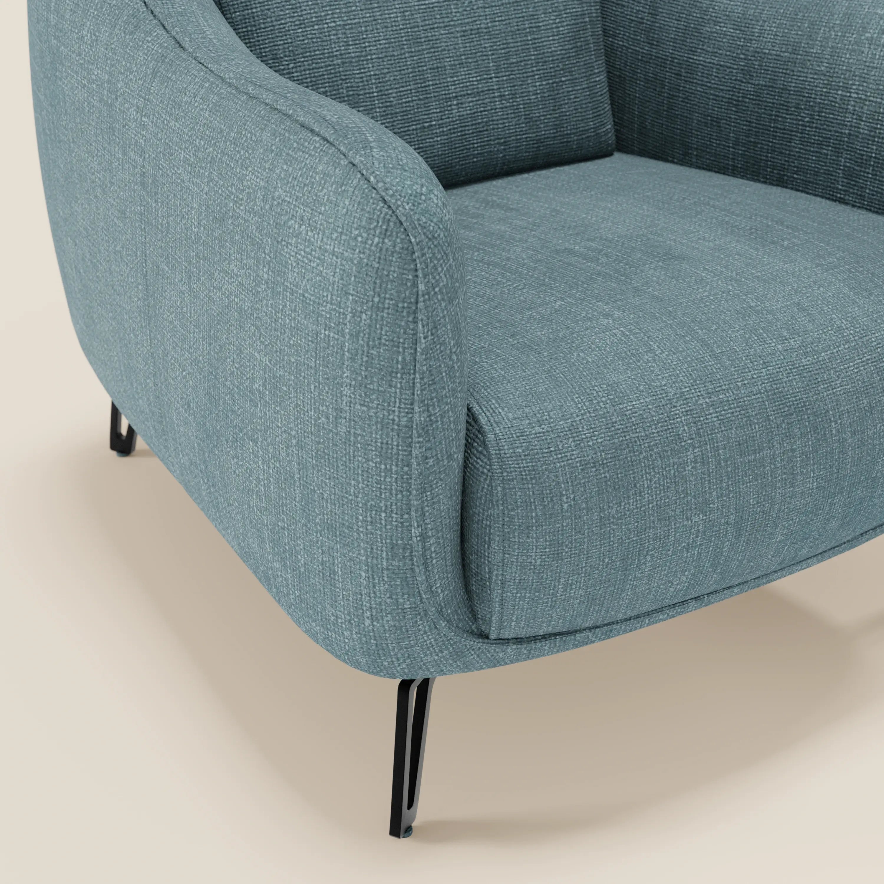 Un primo piano di Avela Poltroncina di Divani.Store mette in evidenza il tessuto impermeabile T06 azzurro, i bordi arrotondati e le sottili gambe in metallo nero su uno sfondo beige chiaro; sono visibili solo parte della seduta, del bracciolo e delle due gambe.