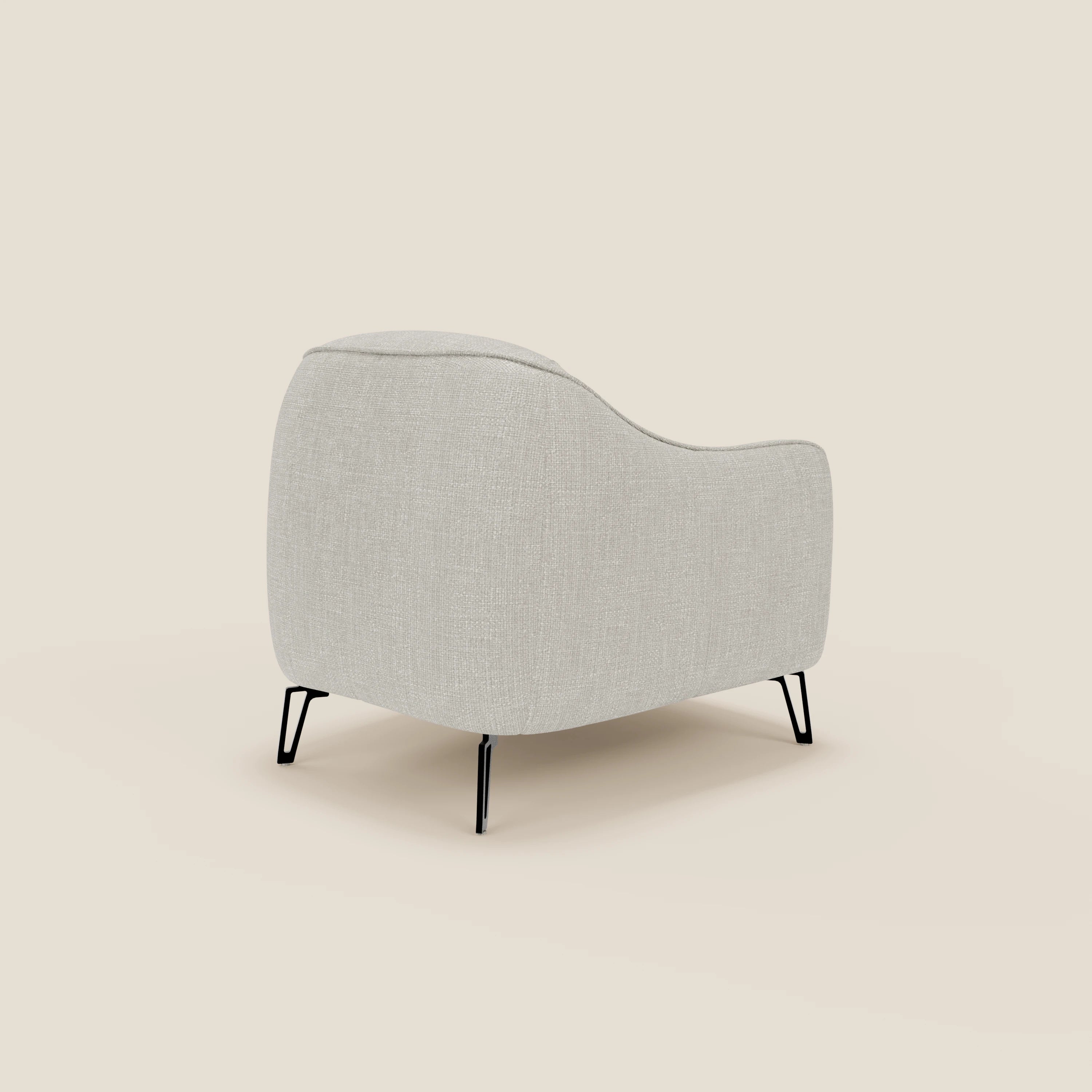 La poltroncina Avela dal comfort senza tempo di Divani.Store in morbido tessuto impermeabile T06 grigio chiaro è vista da dietro con un'angolazione che mette in evidenza i suoi bordi morbidi e arrotondati, lo schienale basso e le sottili gambe in metallo nero su uno sfondo beige.