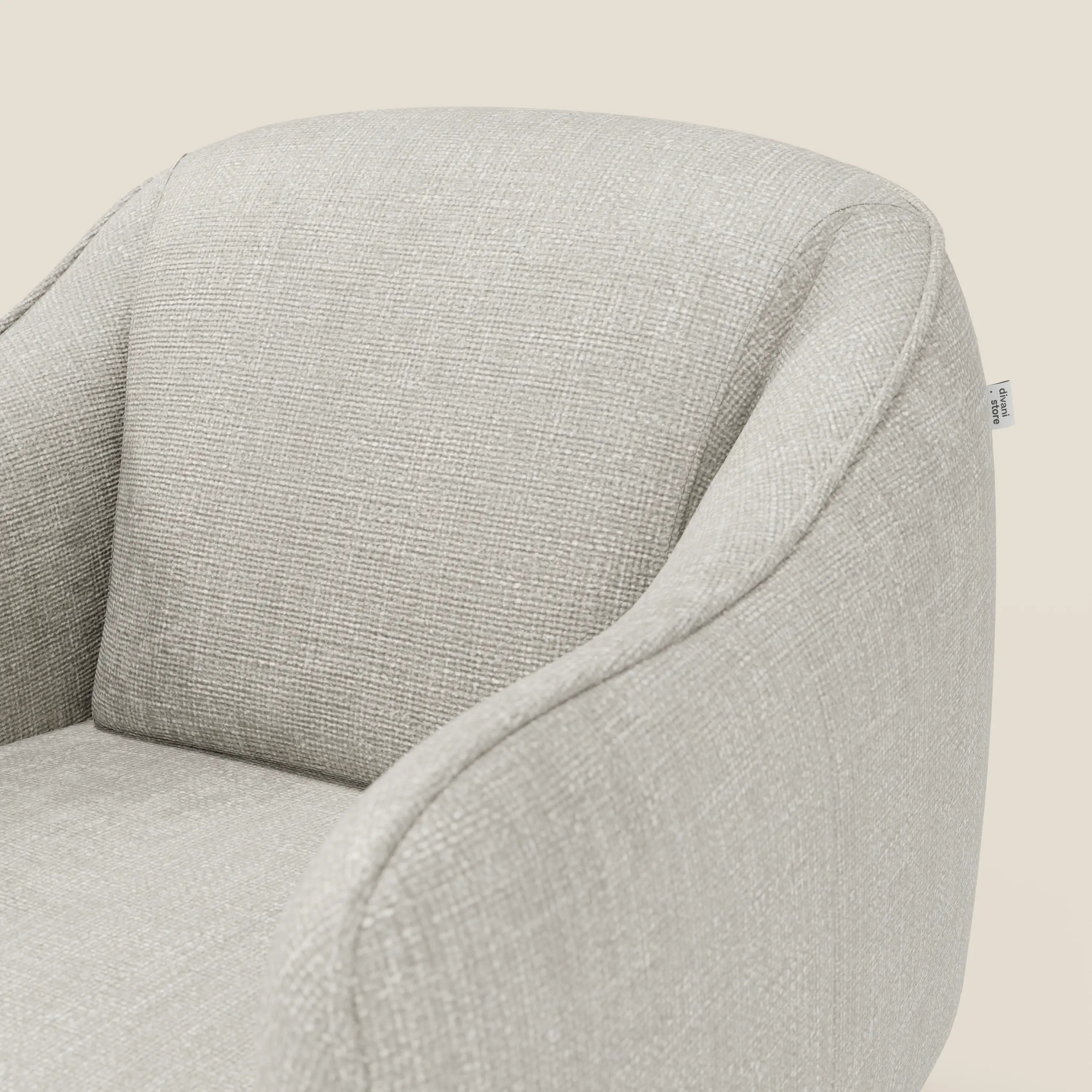 Primo piano di Avela Poltroncina di Divani.Store, rivestita in tessuto impermeabile grigio chiaro T06. Presenta uno schienale arrotondato e braccioli con curve morbide, oltre a una piccola etichetta bianca sul lato. Lo sfondo è di un semplice bianco sporco.
