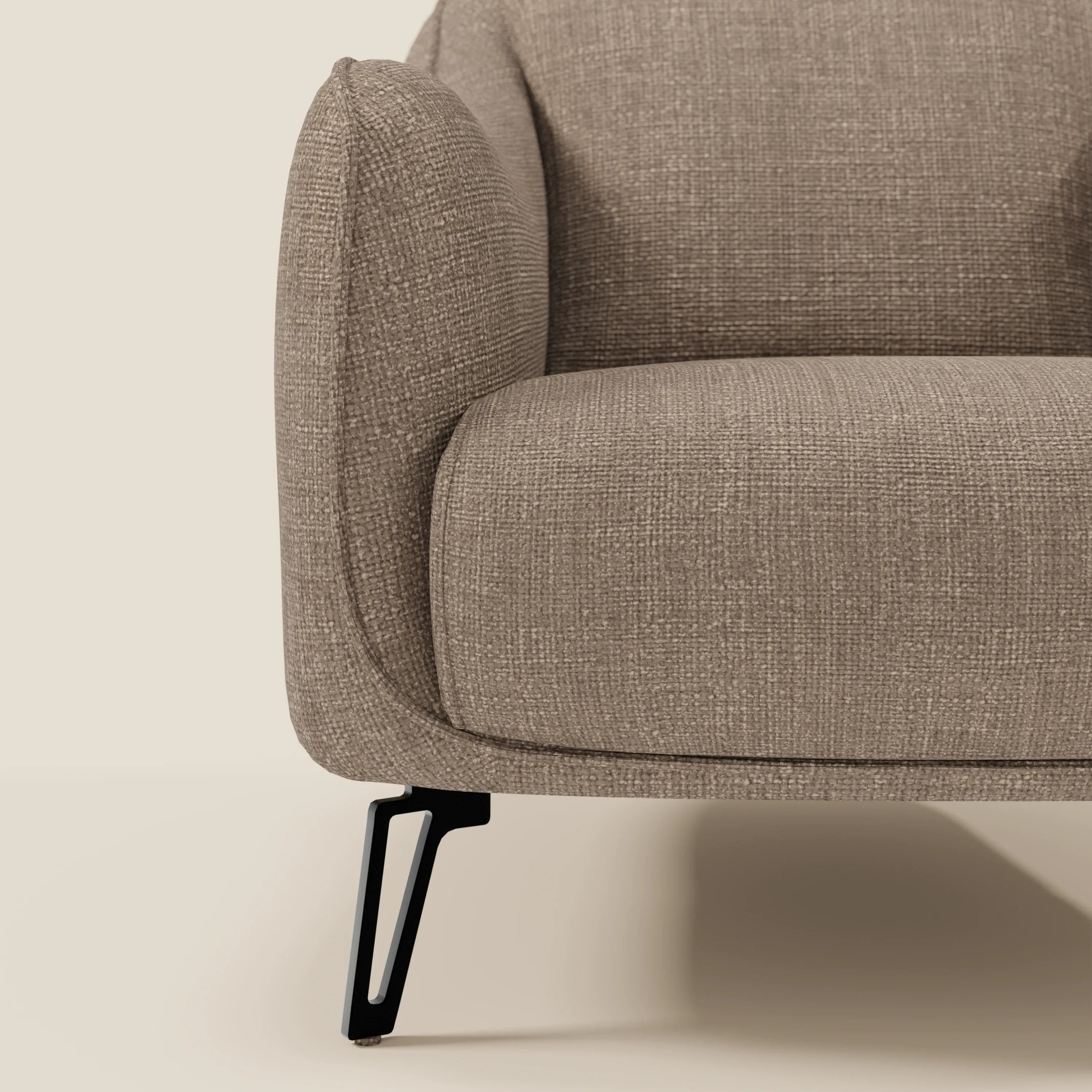Primo piano di Avela Poltroncina di Divani.Store, che mostra il tessuto impermeabile marrone T06, il bracciolo morbidamente arrotondato e la gamba in metallo nero con ritaglio geometrico su sfondo beige.