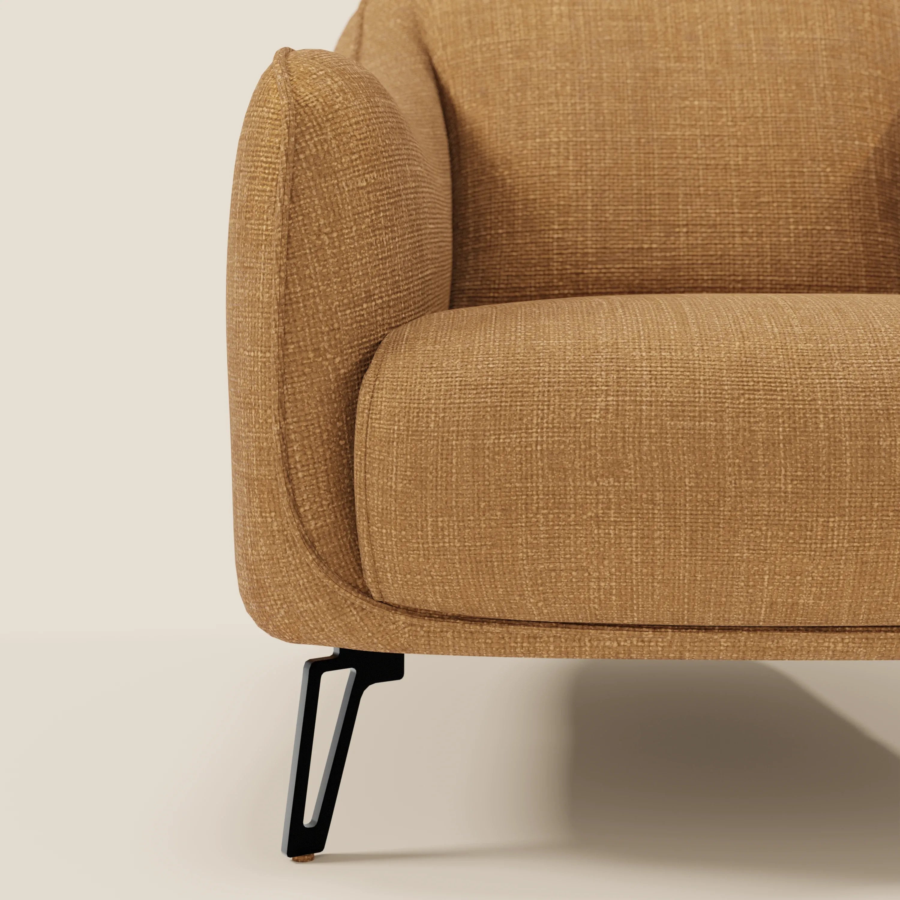 Primo piano di Avela Poltroncina di Divani.Store in morbido tessuto ocra T06, resistente all'acqua, che mette in risalto il moderno bracciolo, la seduta e le eleganti gambe in metallo nero su uno sfondo beige. Il design senza tempo è visibile solo in parte.