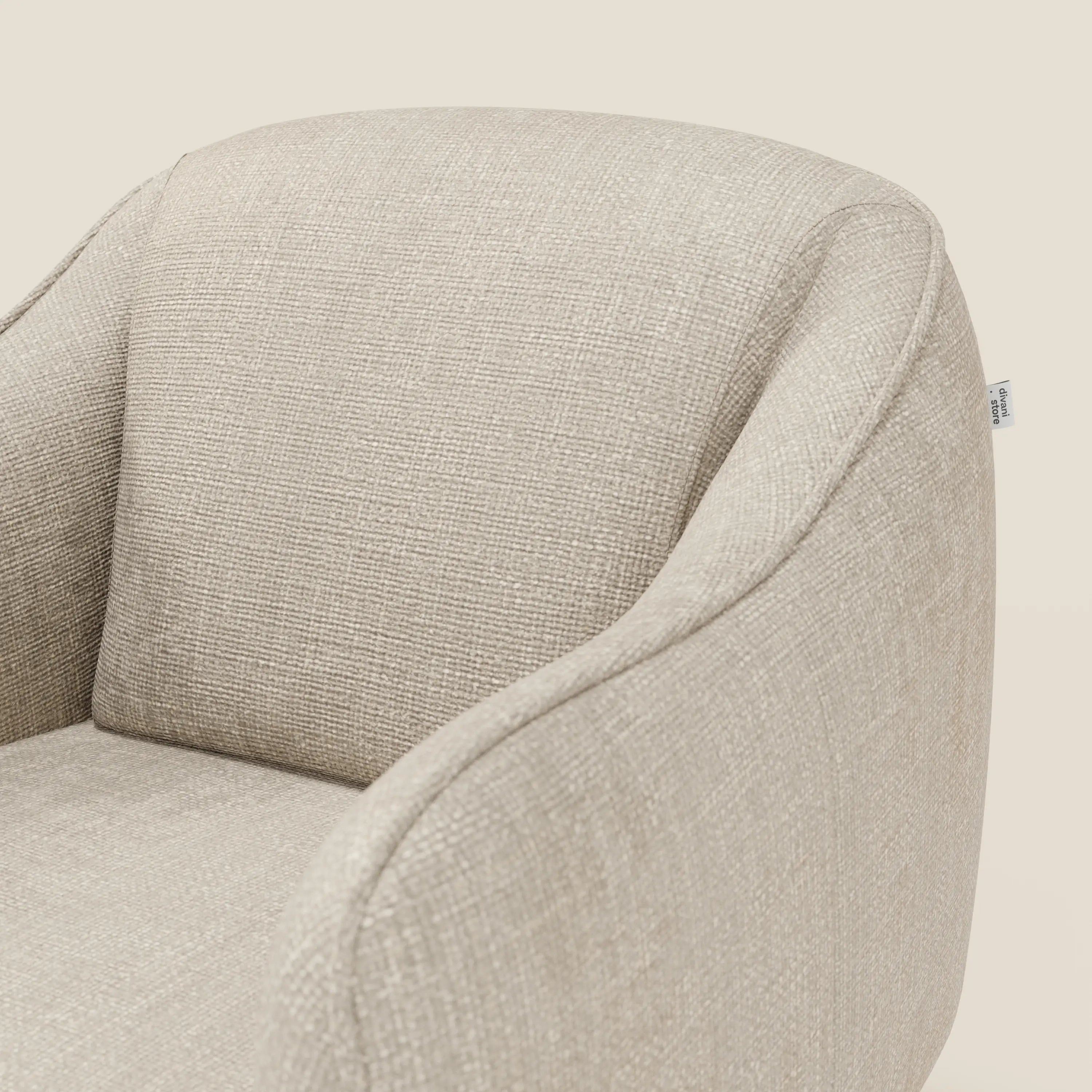 Primo piano di Avela Poltroncina di Divani.Store, caratterizzata da un comfort senza tempo in morbido tessuto panna T06 resistente all'acqua, con braccioli curvi, schienale arrotondato e una sottile etichetta in tessuto su uno sfondo crema chiaro.