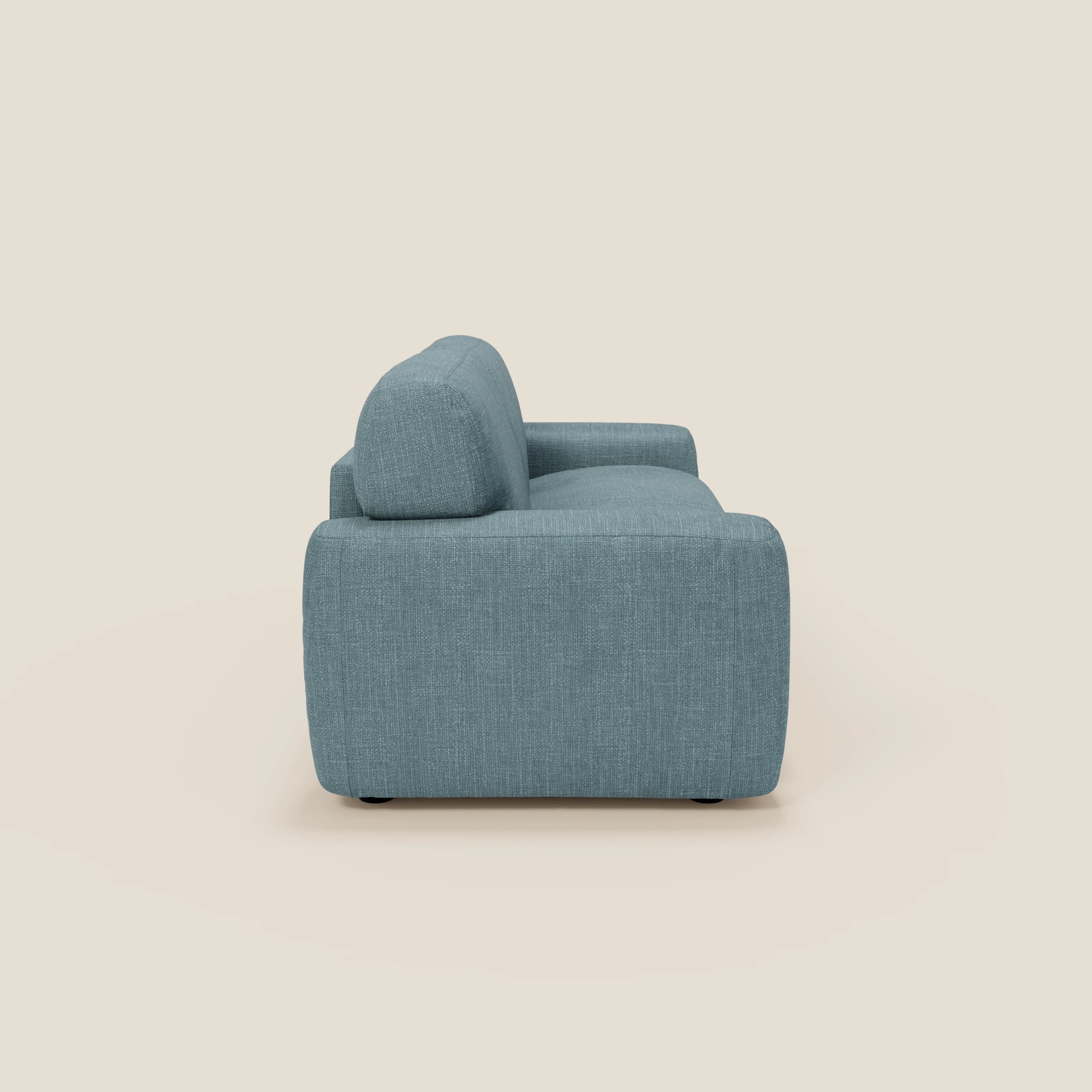 Il letto materasso Cloud Divano H17 cm di Divani.Store, presentato in tessuto impermeabile T06 azzurro, è caratterizzato da un design morbido e arrotondato con un bracciolo e uno schienale imbottito, che incarna il comfort quotidiano su uno sfondo beige chiaro.