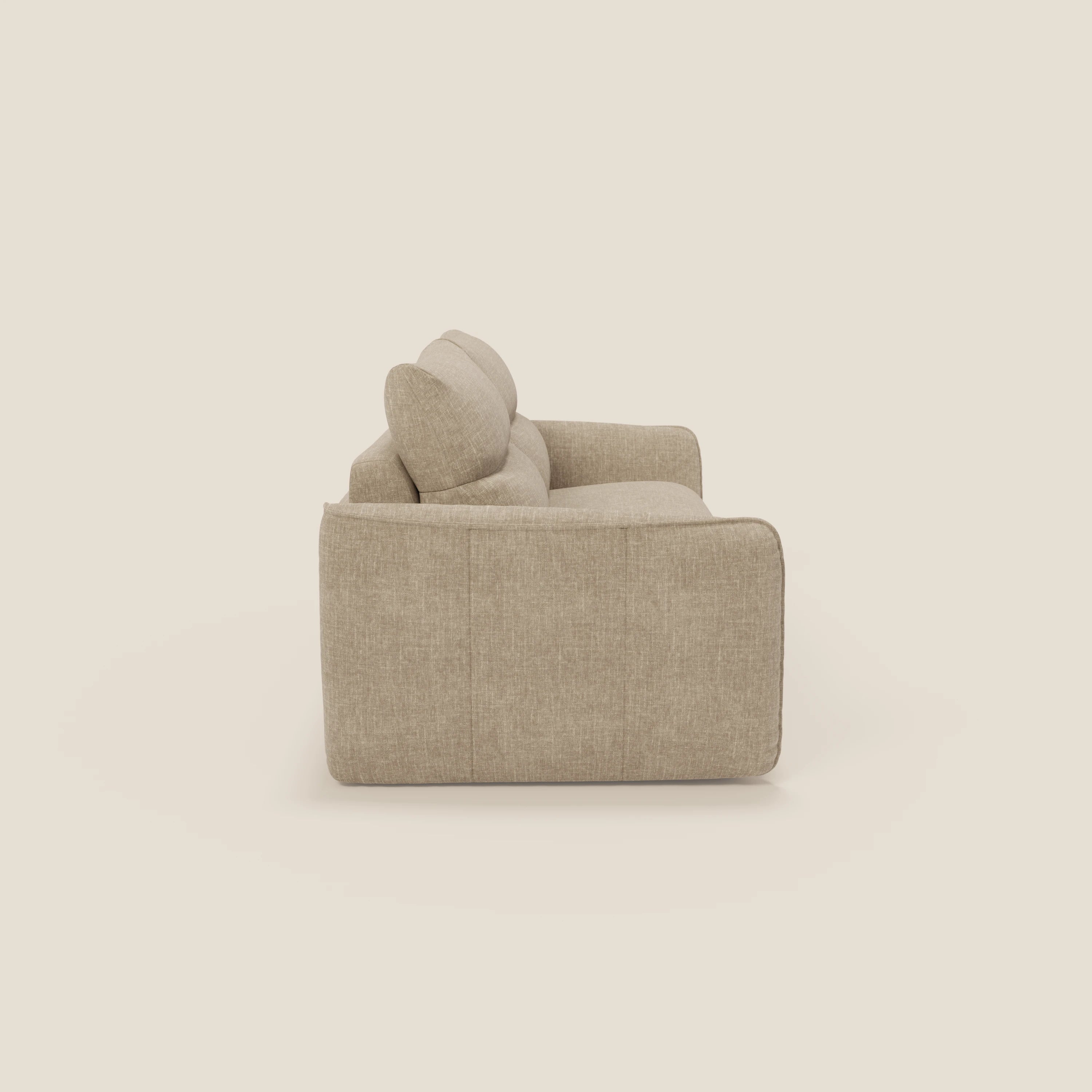 Vista laterale del divano letto Elios Divano con morbidi cuscini spalliera in tessuto smacchiabile T24 beige di Divani.Store, caratterizzato da una moderna forma squadrata, cuscini in peluche e morbidi bordi arrotondati, su uno sfondo bianco sporco.