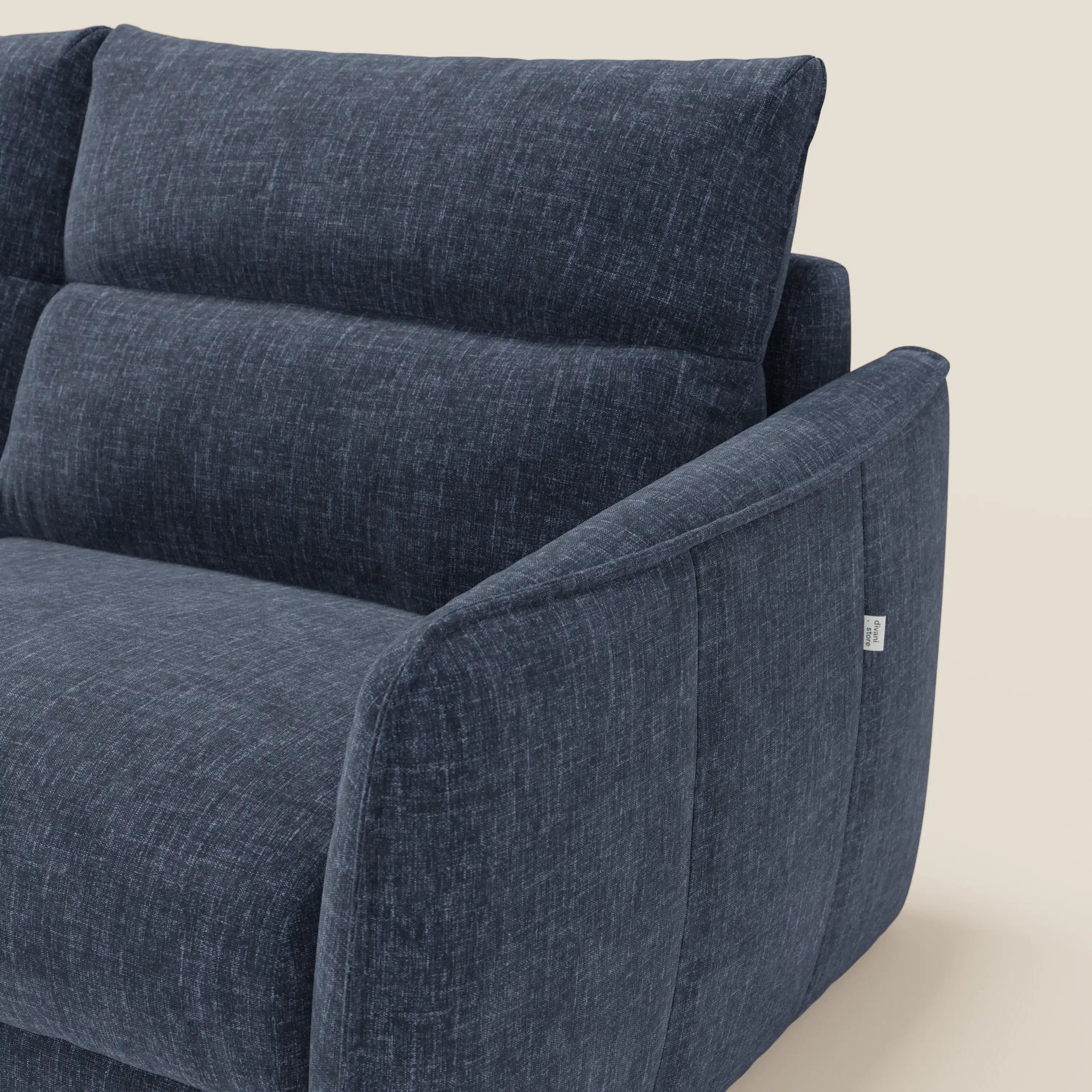 Primo piano del Divano letto Elios di Divani.Store, caratterizzato da cuscini a spicchi e braccioli angolari in tessuto antimacchia T24 blu, con targhetta bianca sul lato. Lo sfondo è un semplice beige chiaro.