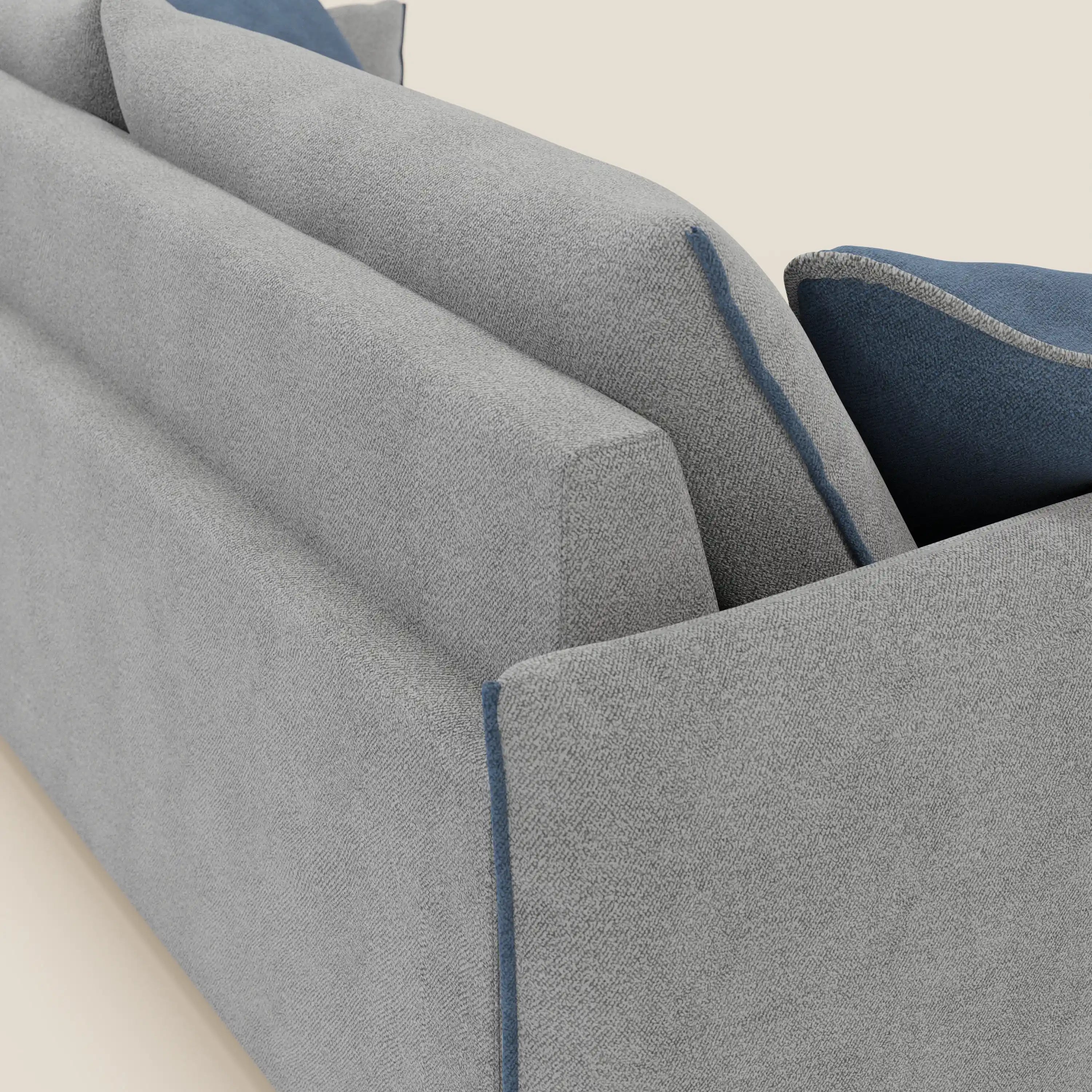 Primo piano del divano Flexar con sedute allungabili e schienale in piuma di Divani.Store, presentato in morbido bouclé impermeabile T07 grigio-blu. Due cuscini d'accento blu con profili a contrasto e piuma d'oca si appoggiano allo schienale. Fondo bianco sporco.