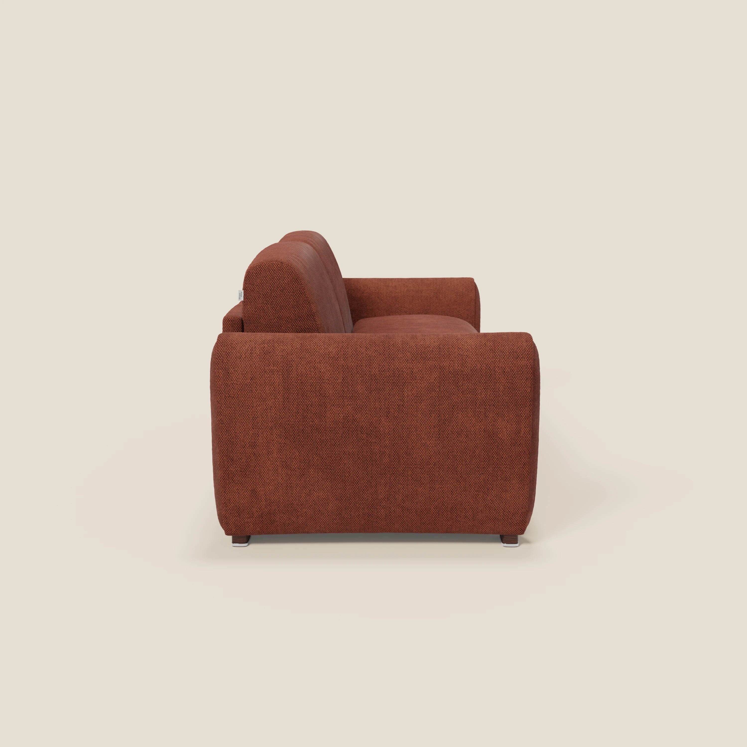 Il Kaleo Divano letto moderno di Divani.Store, in tessuto impermeabile T26 arancione ruggine e materasso H17 cm alta densità, è mostrato di lato su sfondo beige chiaro, con ampi braccioli e design contemporaneo.
