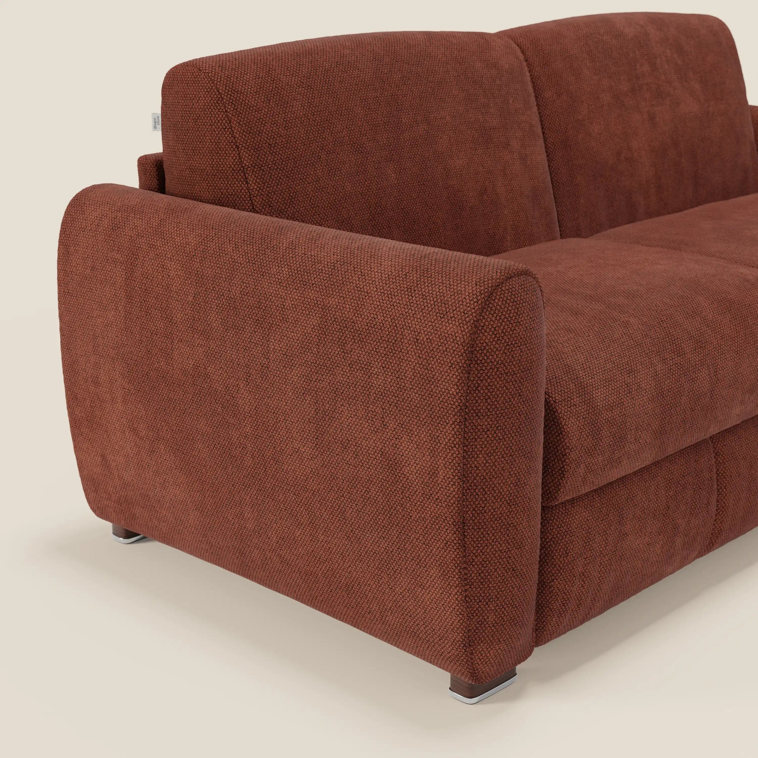 Primo piano del divano letto moderno Kaleo di Divani.Store, caratterizzato da braccioli spessi e arrotondati, tessuto impermeabile T26 arancione ruggine, gambe in metallo e materasso H17 cm, su uno sfondo beige semplice con cuscini parzialmente visibili.