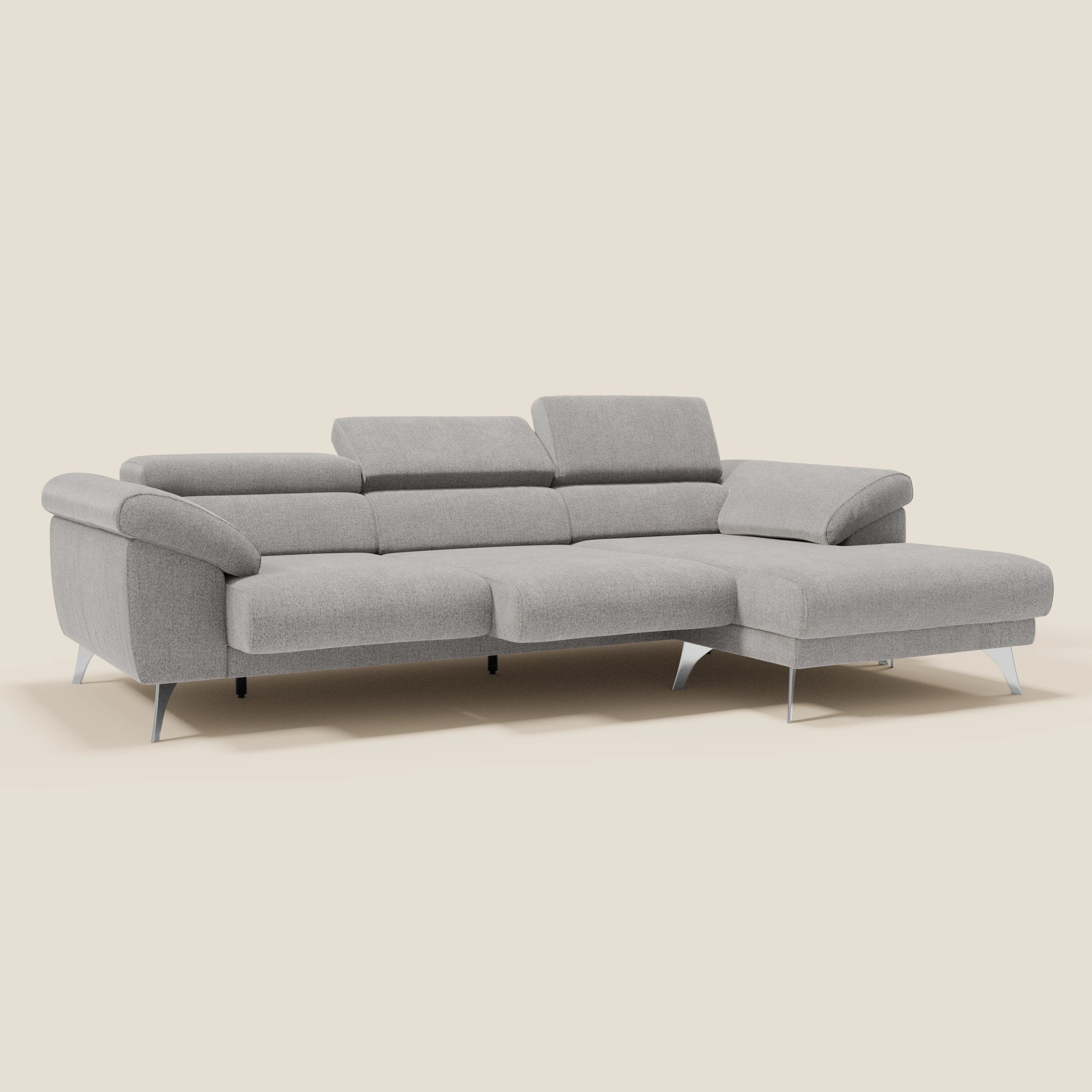 Il Divano angolare Donatello di Divani.Store è caratterizzato da sedute scorrevoli, braccioli portaoggetti e poggiatesta regolabili in tessuto antimacchia T23 grigio chiaro, con una chaise lounge sul lato destro su uno sfondo beige semplice.