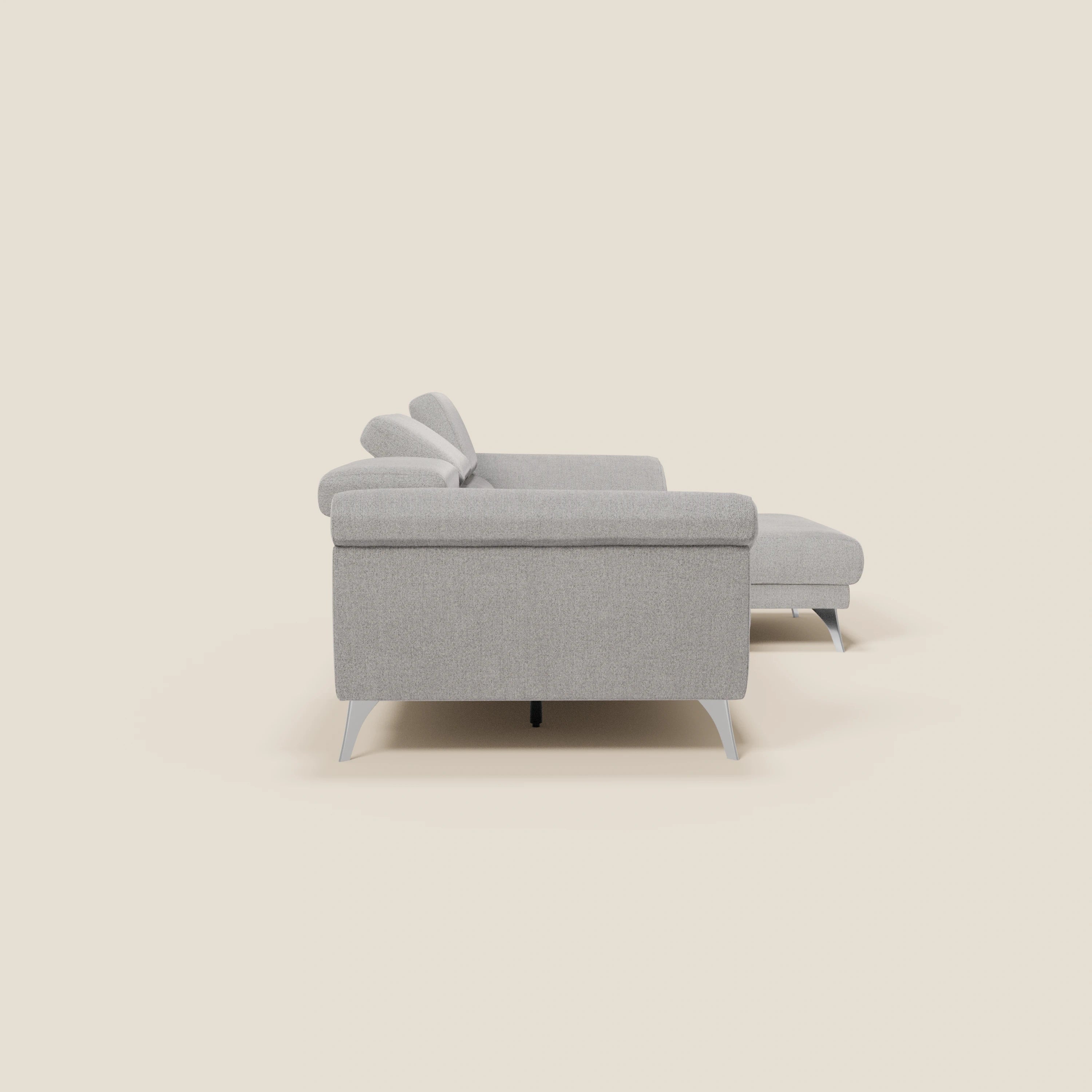 Una vista laterale mostra il Donatello Divano angolare di Divani.Store in tessuto antimacchia T23 grigio chiaro, con sedute scorrevoli, braccioli portaoggetti e chaise longue a destra. Il fondo bianco sporco esalta il design minimalista di Confort Evoluto.